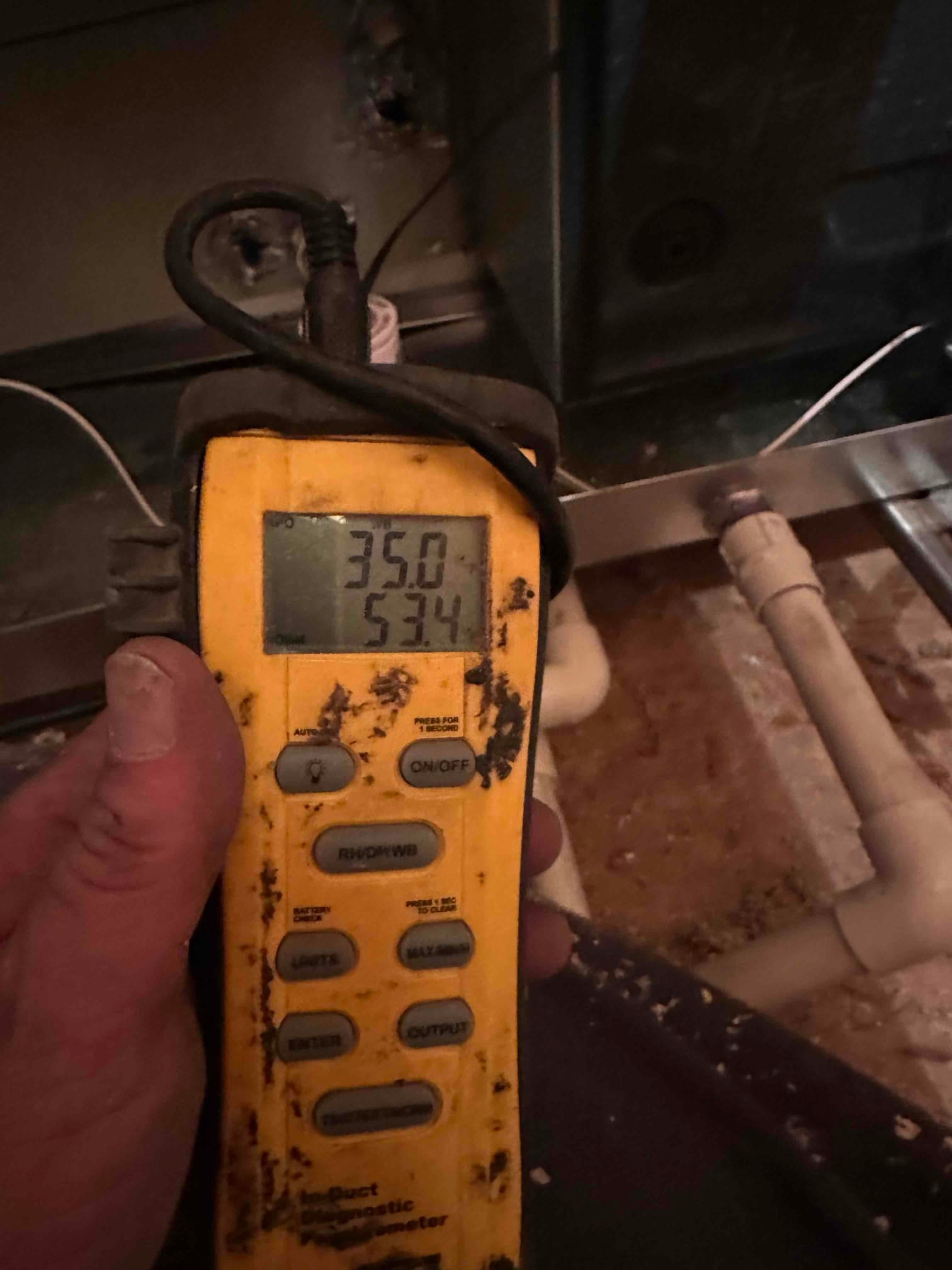 Handheld digital thermometer shows 53.4 degrees Fahrenheit while measuring air temperature near the indoor unit.
