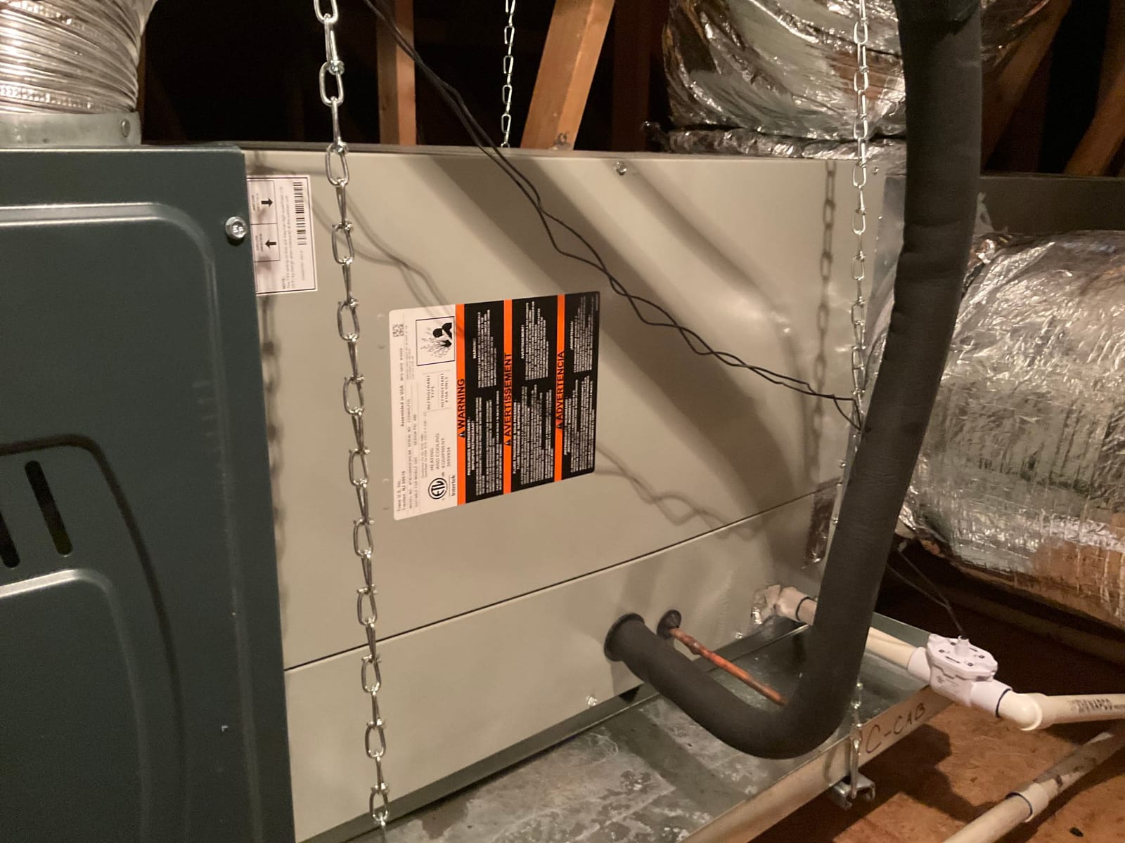 Horizontal air handler hung from chains in attic with insulated refrigerant lines and PVC condensate drain connected.