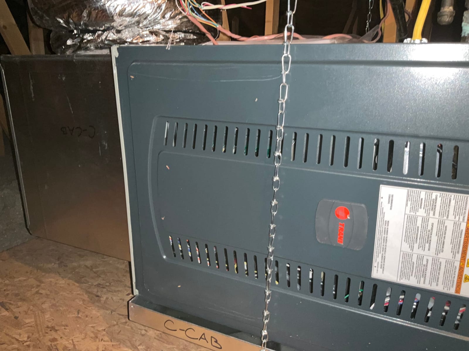 Horizontal air handler suspended in attic with duct connection and hanging chains visible during installation.