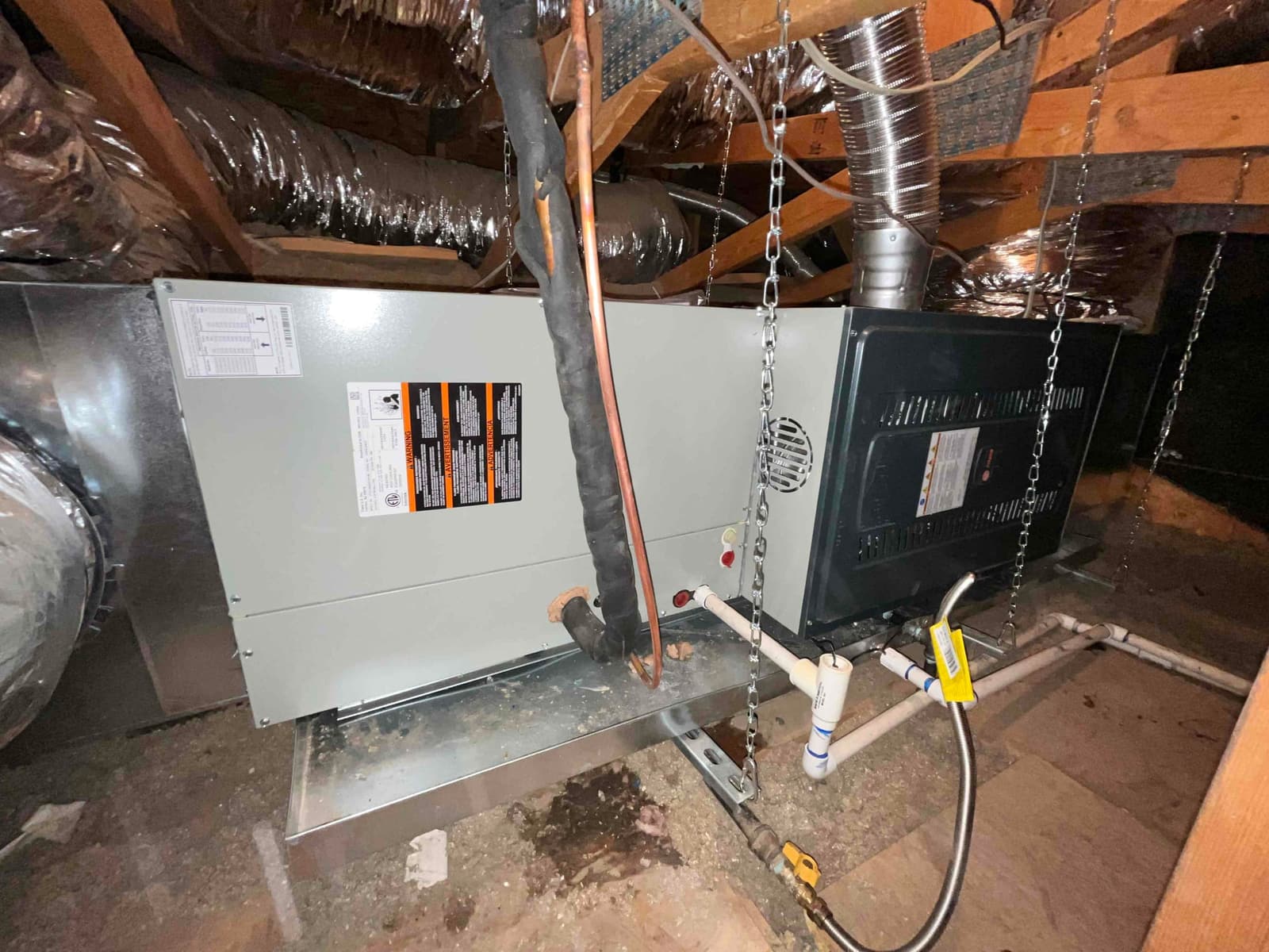 Horizontal furnace and coil assembly hung in attic with gas connection, condensate drain, insulated refrigerant lines, and duct connections completed.