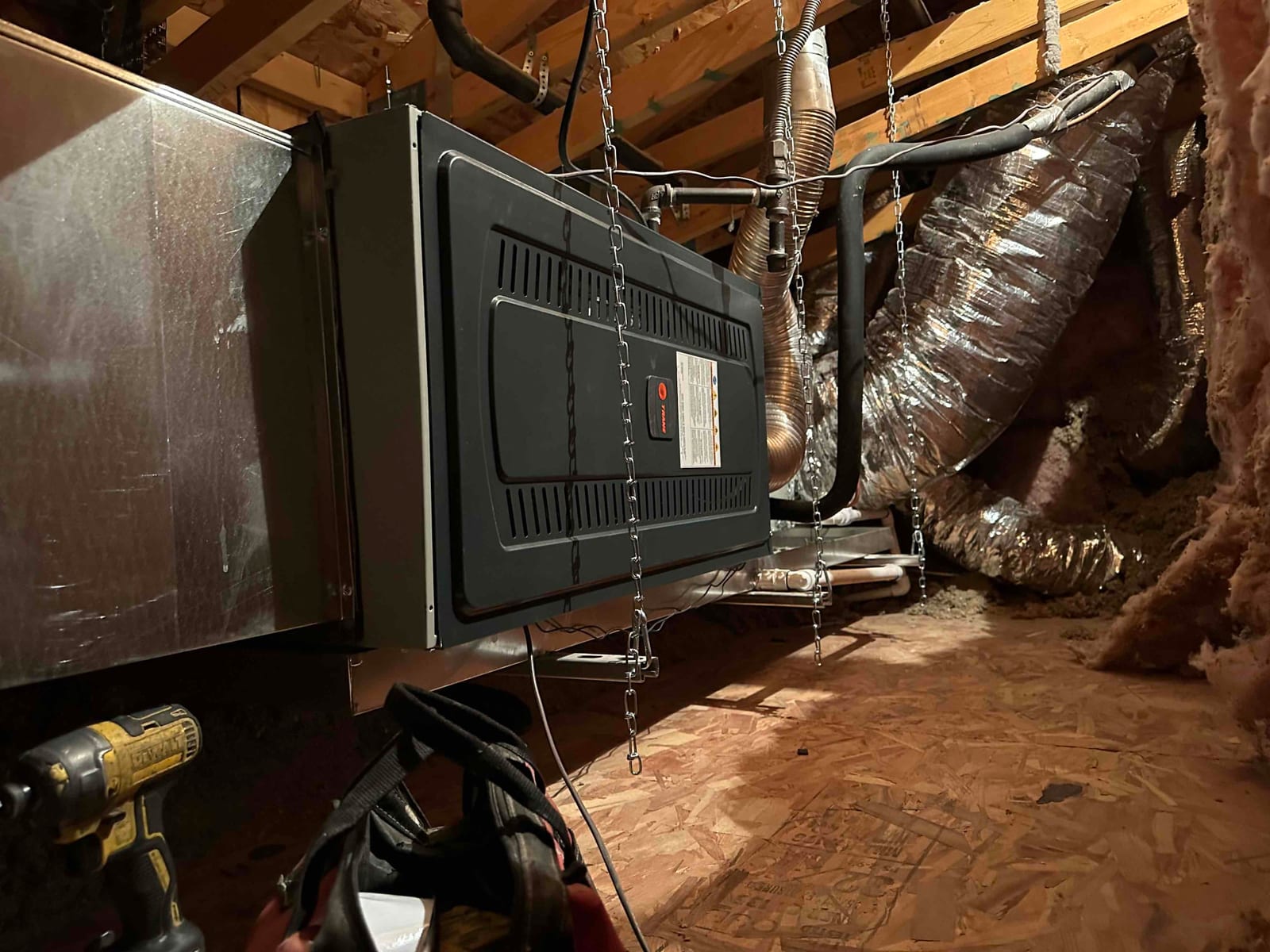 Horizontal furnace and coil suspended from rafters with chains, connected to new ductwork, condensate drain, and insulated refrigerant lines.