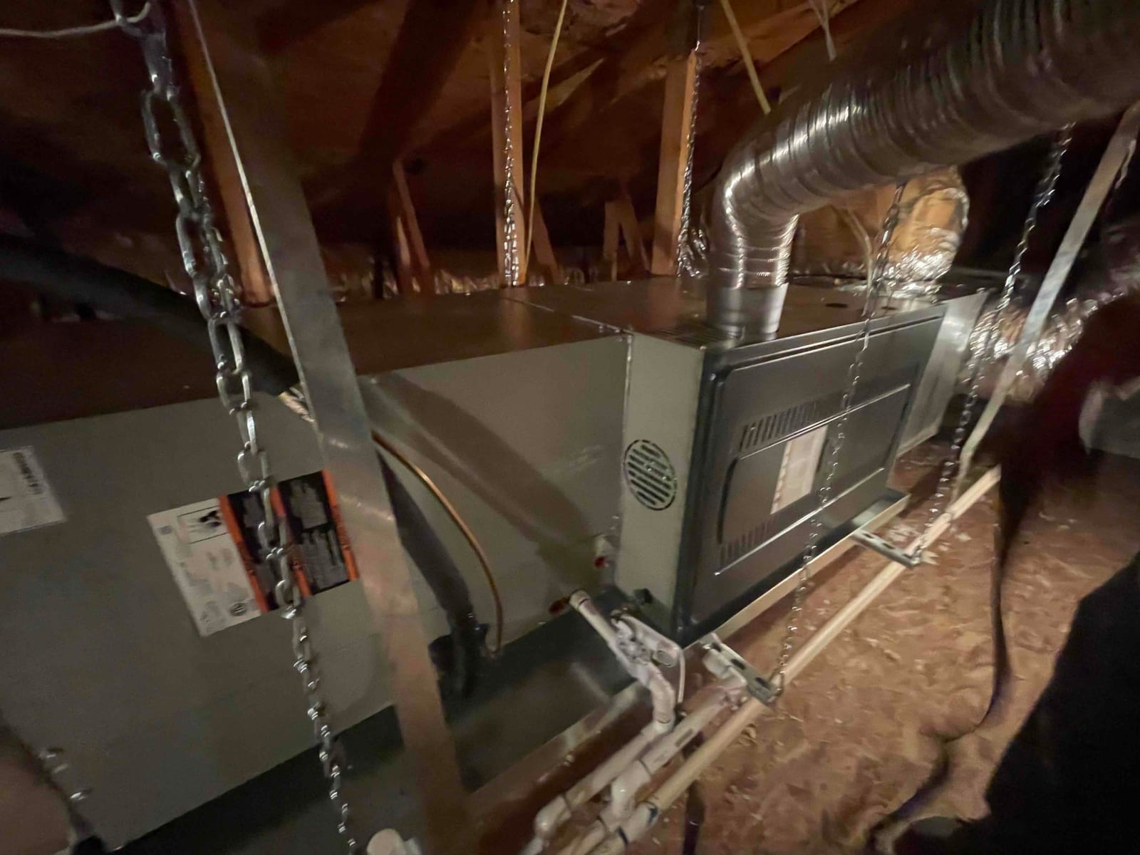 Horizontal gas furnace and coil assembly hung in attic with duct connection, condensate drain piping, and support chains installed.