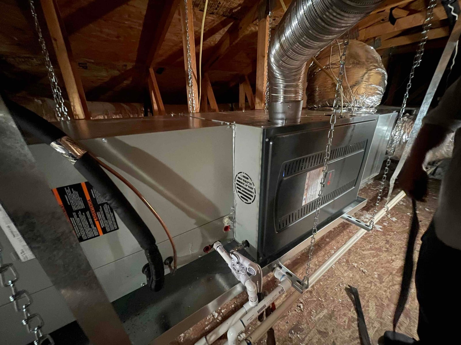 Horizontal gas furnace and coil assembly suspended in attic with condensate drain, insulated refrigerant lines, and duct connections secured.