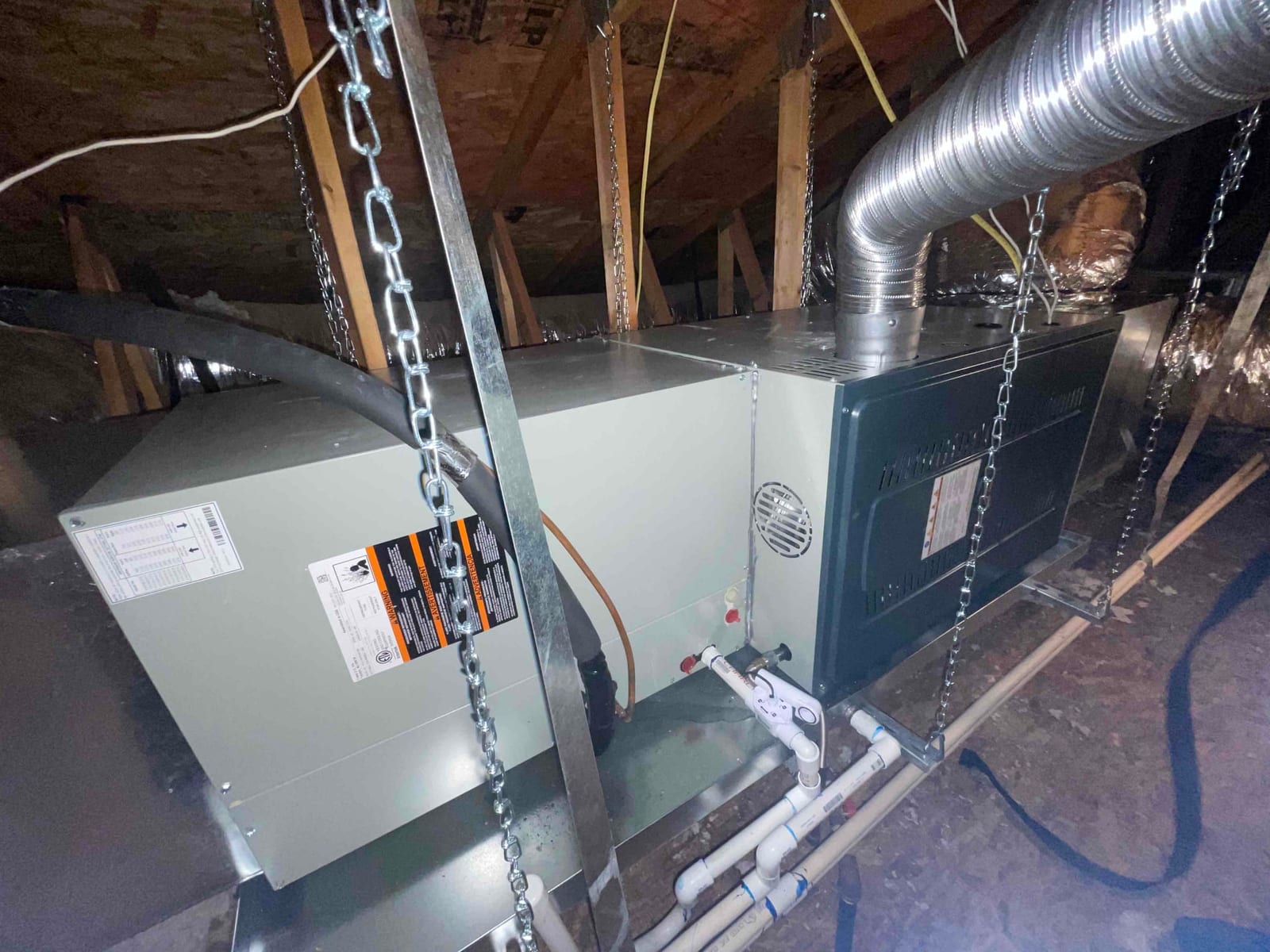 Horizontal gas furnace and evaporator coil suspended with chains in attic, with PVC condensate drain and flexible duct connections installed.