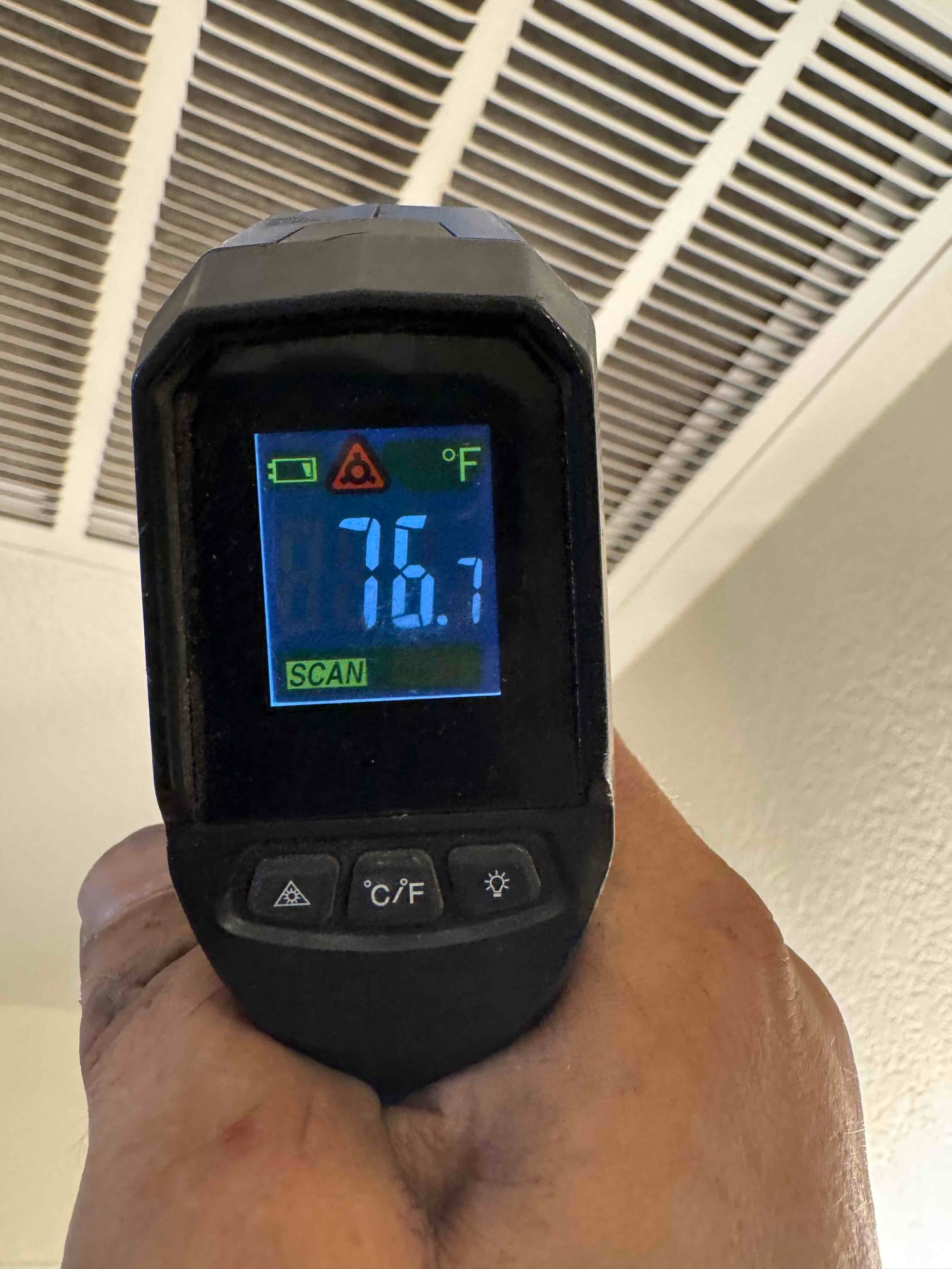 Infrared thermometer aimed at a ceiling return grille shows 76.7°F during airside commissioning.