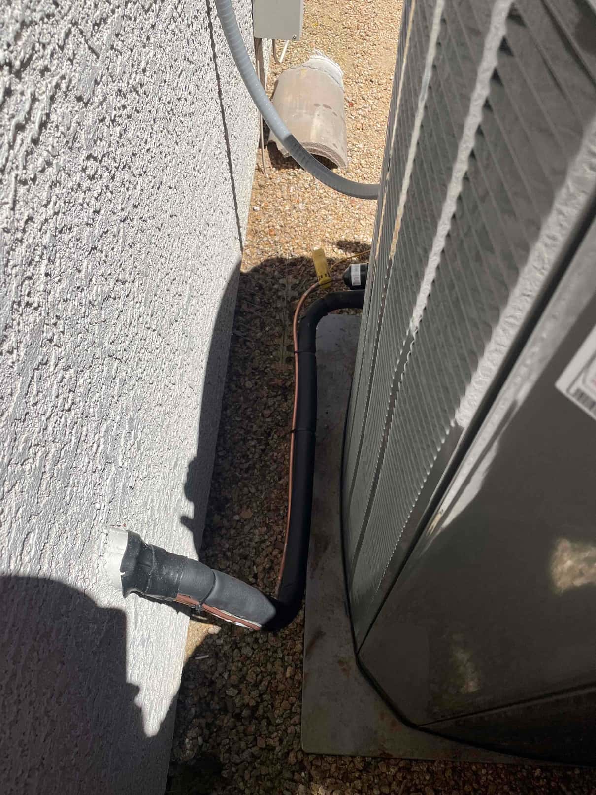 Insulated refrigerant line set exits the wall and connects to the outdoor condenser on a level pad.