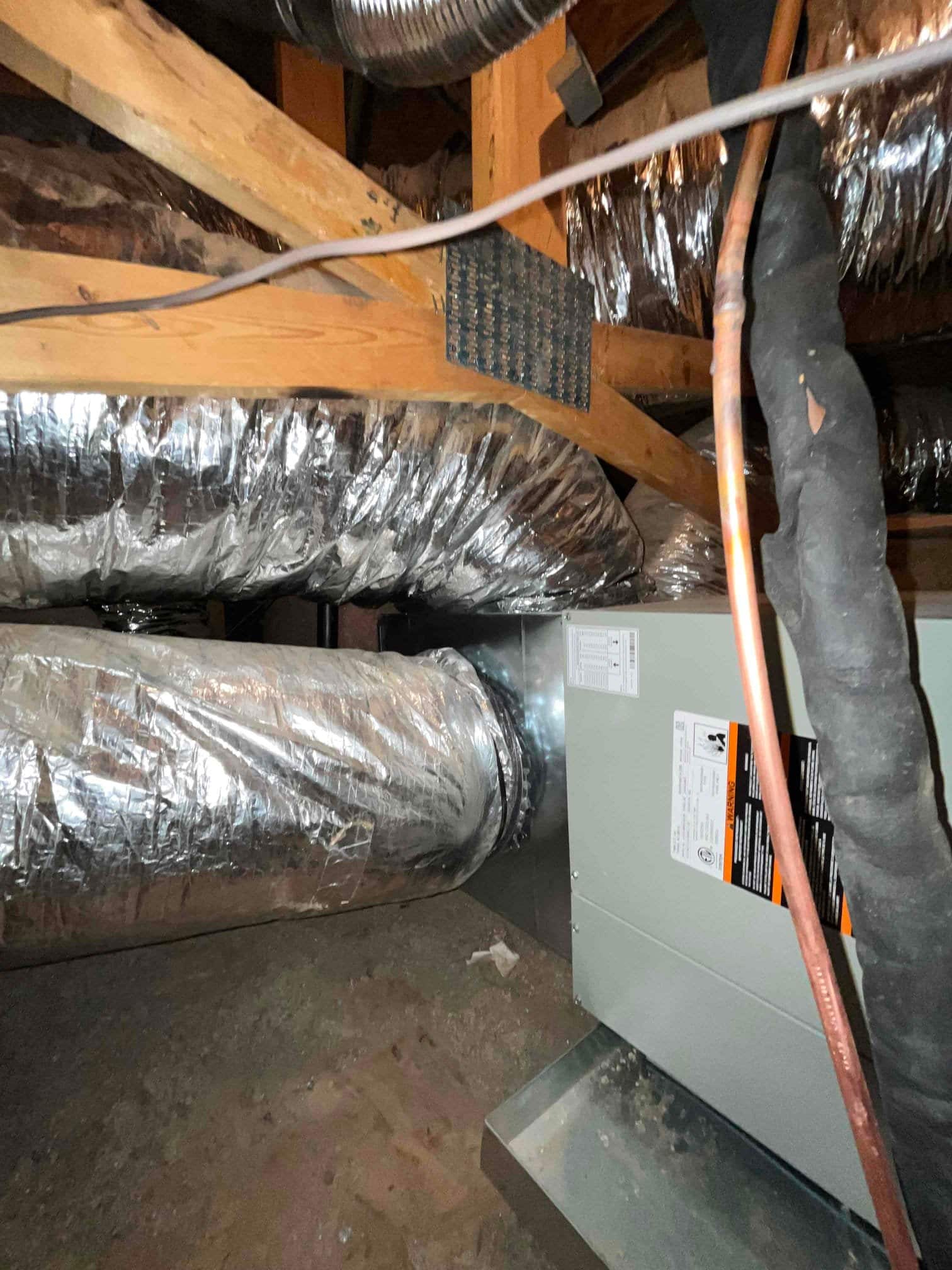 New air handler connected to insulated flex duct in attic, with sealed metal plenum and refrigerant lines routed alongside.