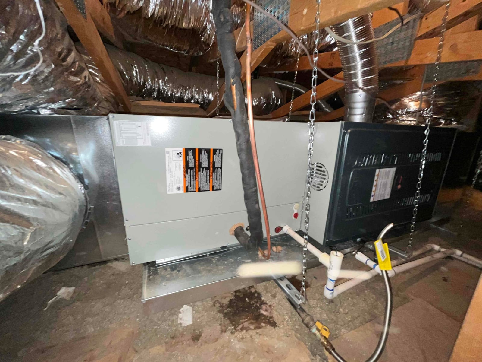 New air handler and furnace assembly suspended in attic with insulated duct connections, condensate drain piping, and gas shutoff valve installed.