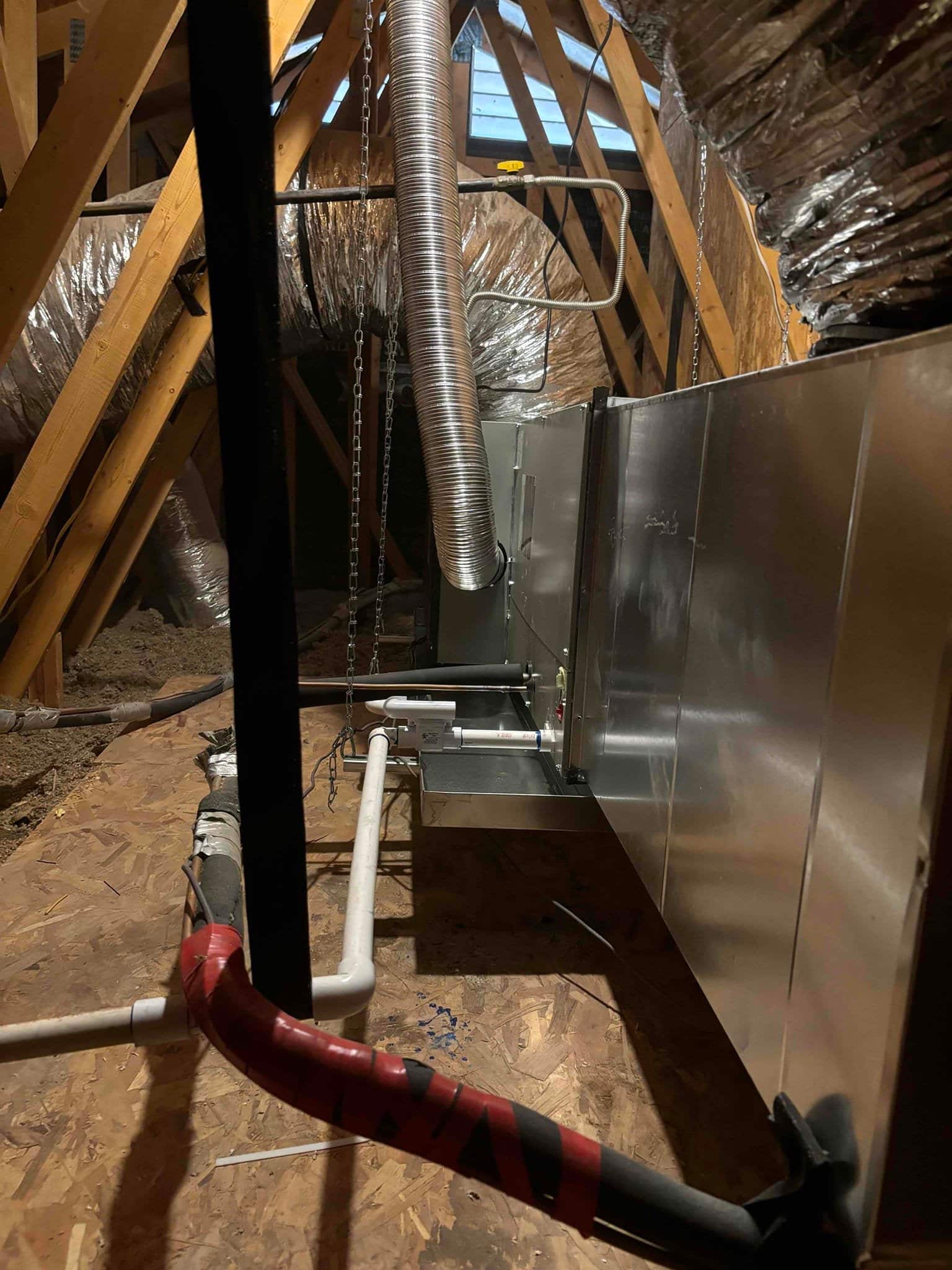New attic air handler installed with insulated flex ducts, condensate drain piping, secondary pan switch, and suspended venting in place.