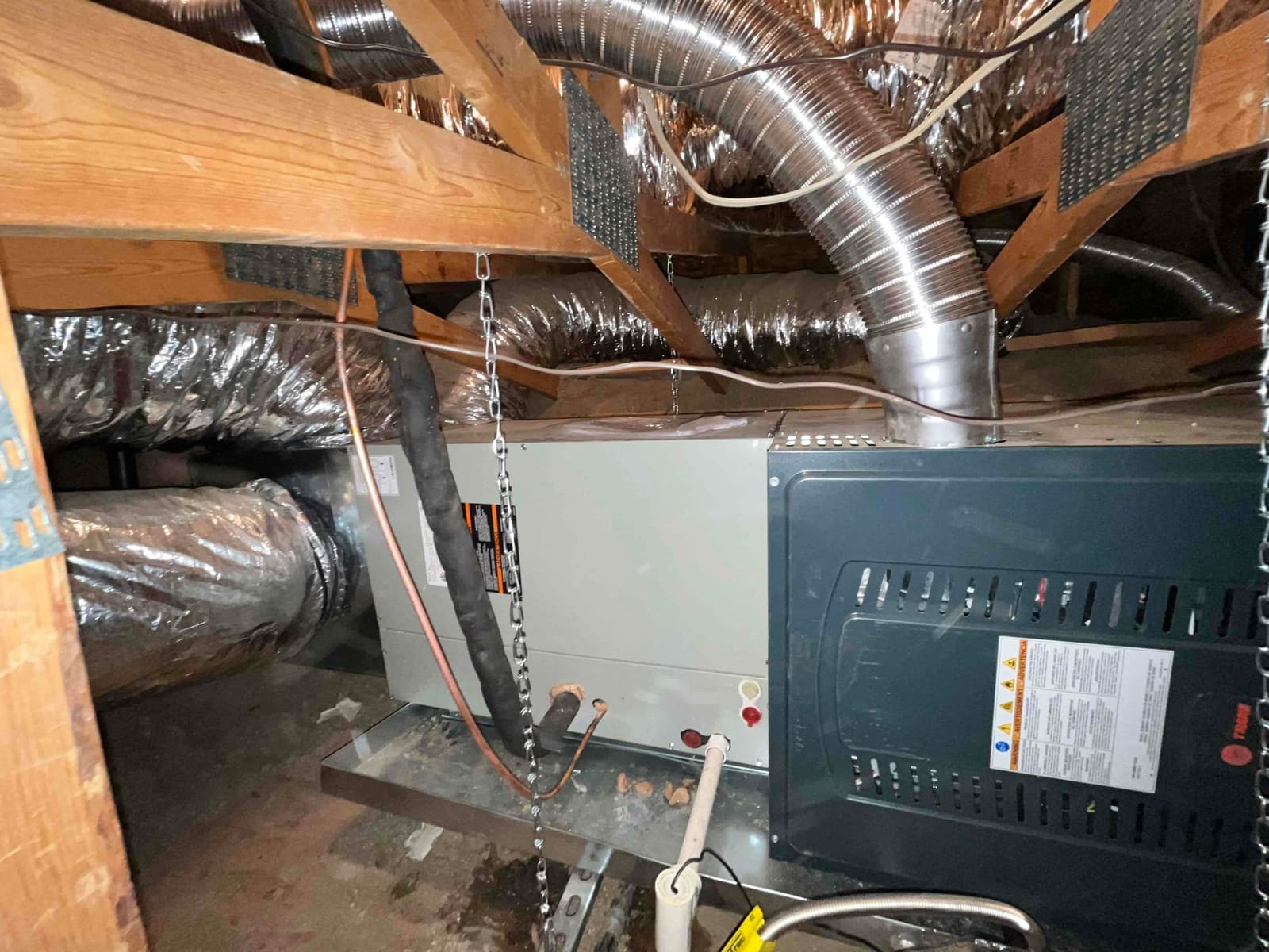 New attic furnace and evaporator set on a drain pan with connected insulated ductwork, gas vent, and condensate drain.