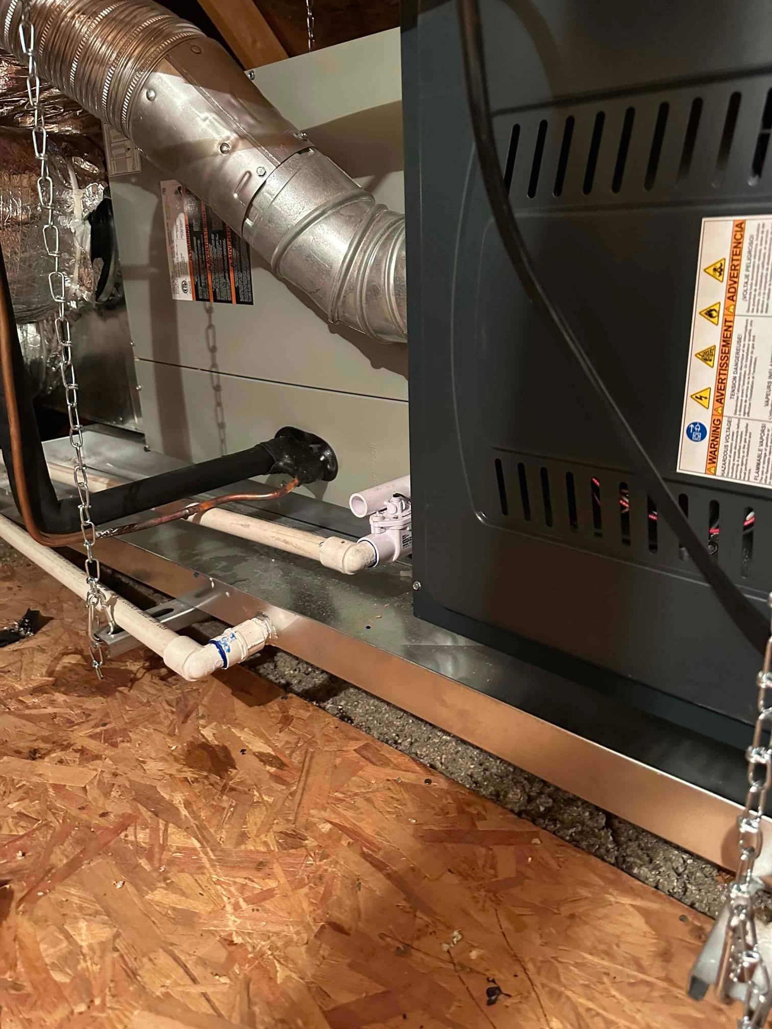 New furnace and coil set in attic with metal venting, insulated refrigerant line, PVC condensate drains, and overflow pan on suspension chains.