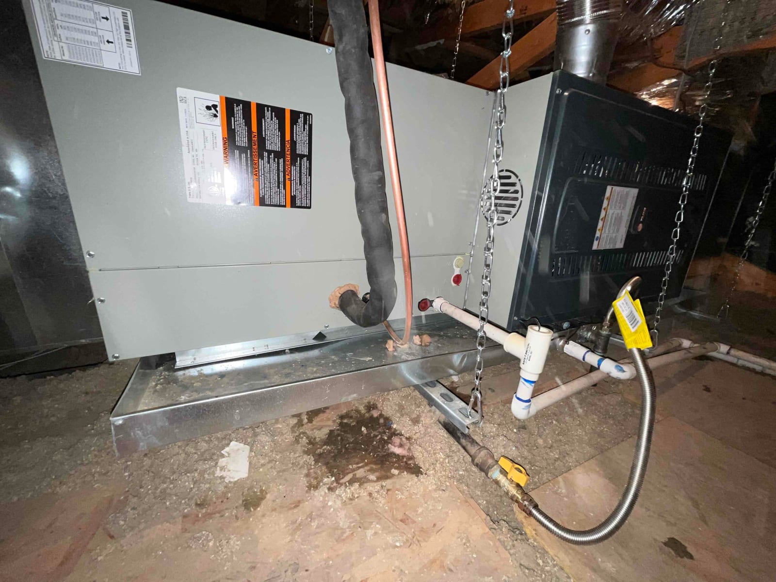 New furnace and coil set on a drain pan with insulated refrigerant lines, condensate piping, gas flex connector, and hanging support chains.