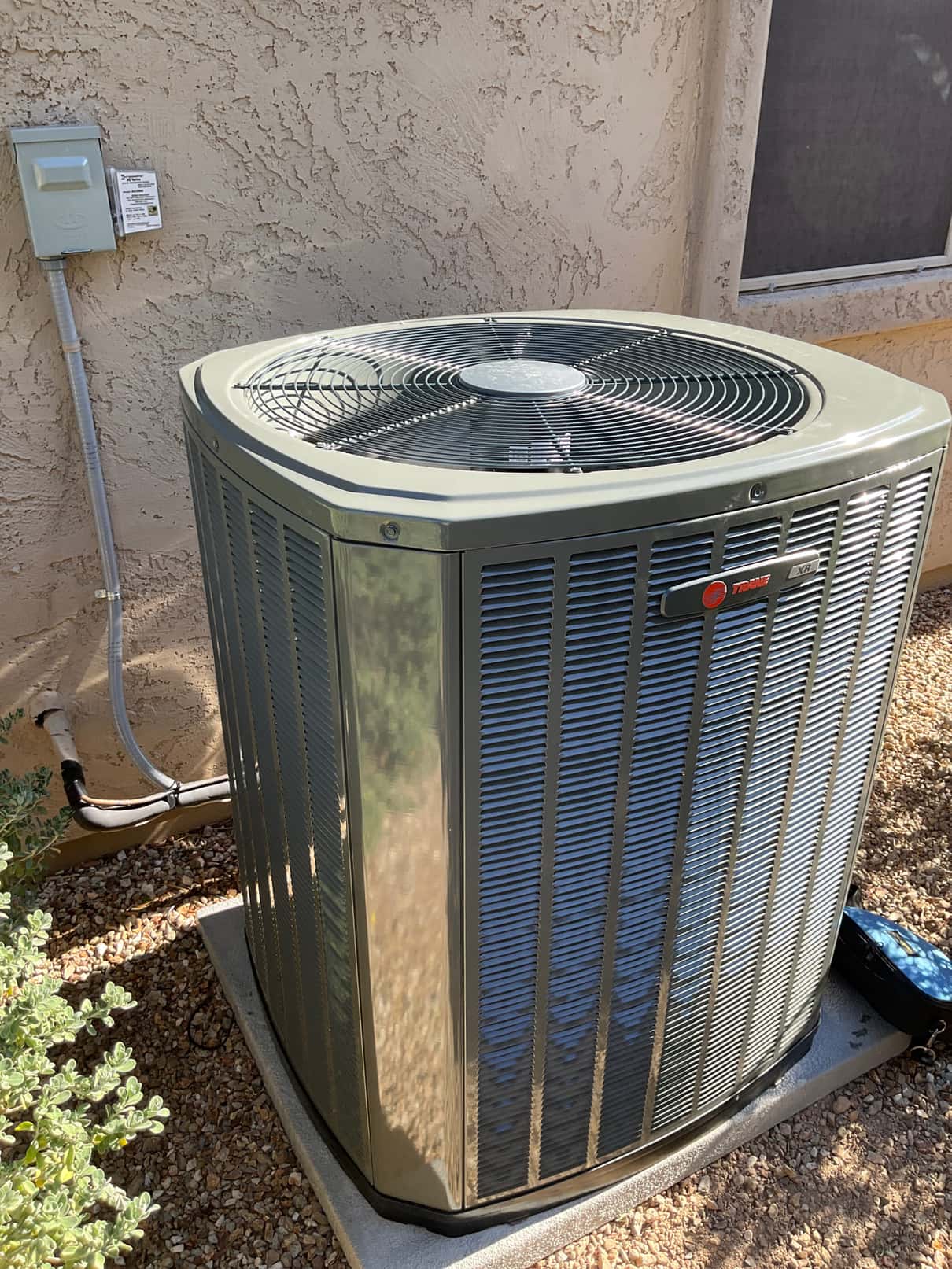 New outdoor condenser set on a level pad with electrical disconnect mounted nearby and insulated refrigerant lines routed to the wall.