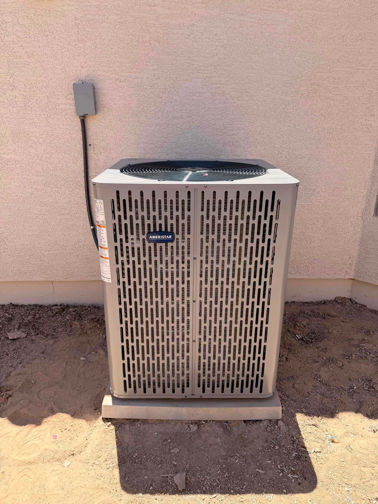 New outdoor condenser set on a level pad with electrical disconnect mounted on the wall beside it.