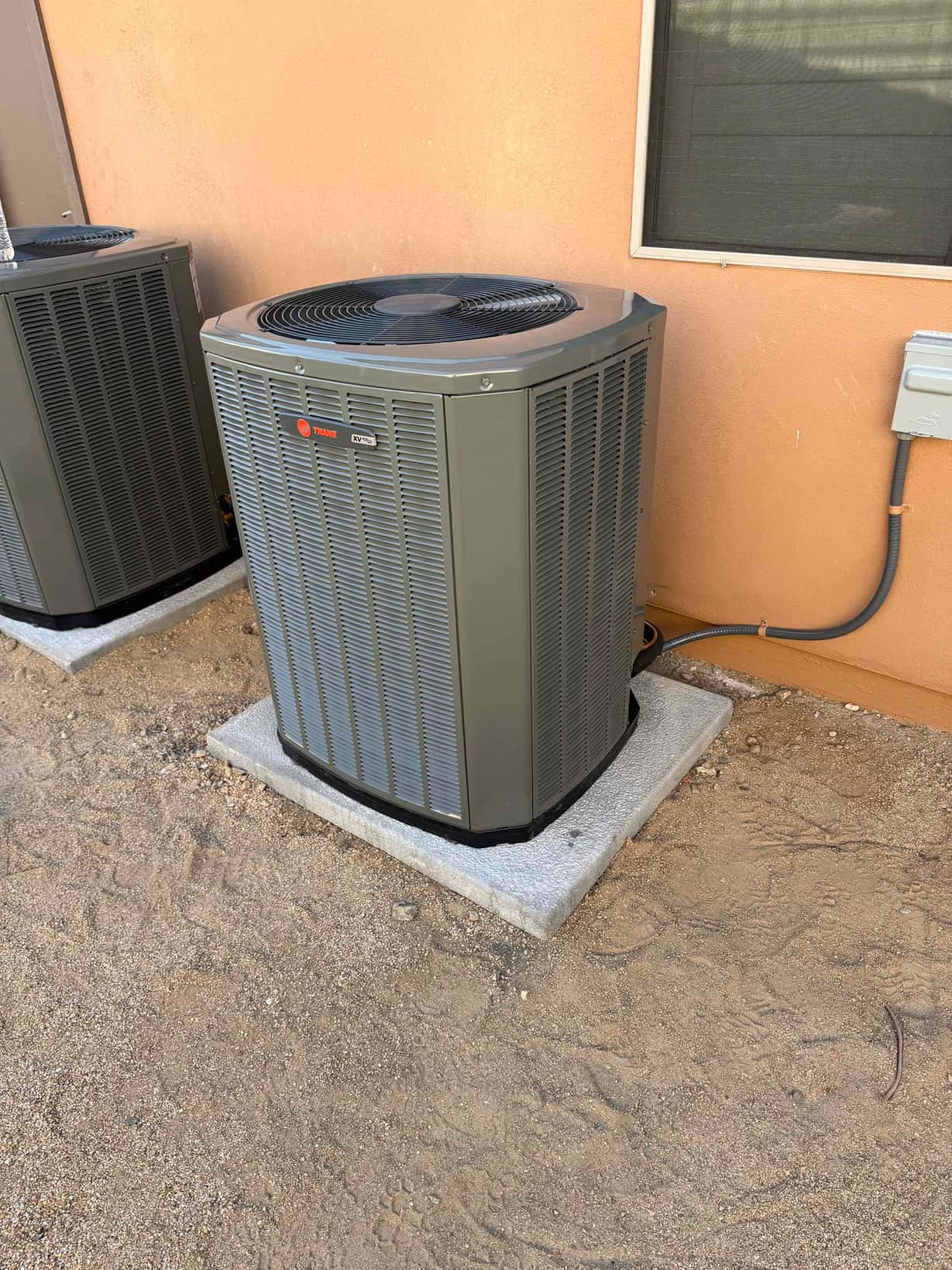 New outdoor condenser set on a level pad with electrical whip and disconnect mounted on the wall nearby.