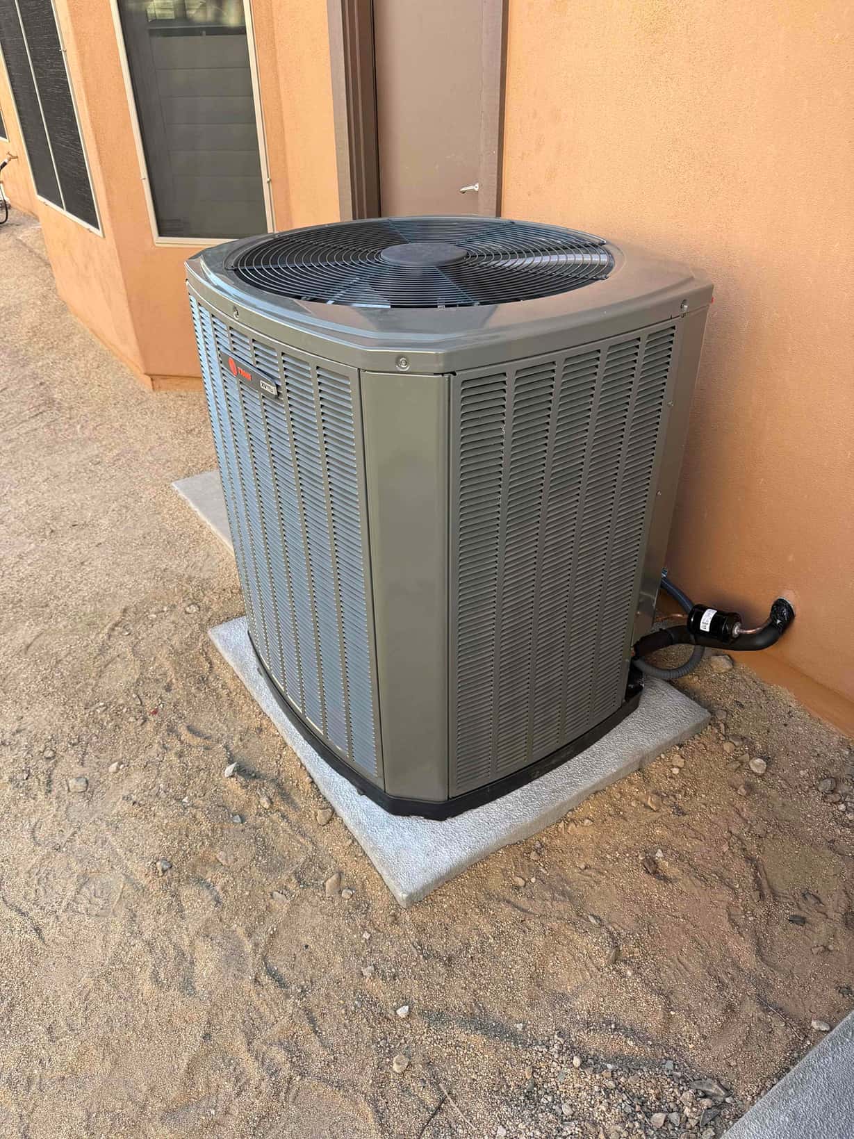 New outdoor condenser set on a level pad with insulated refrigerant lines routed into the wall penetration.