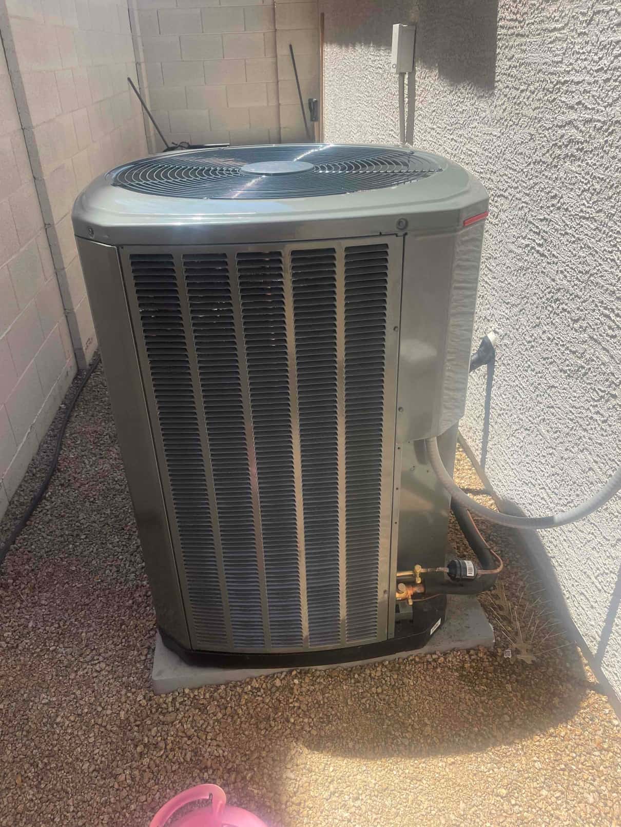 New outdoor condenser set on a level pad with insulated refrigerant lines connected and electrical whip routed to the disconnect.