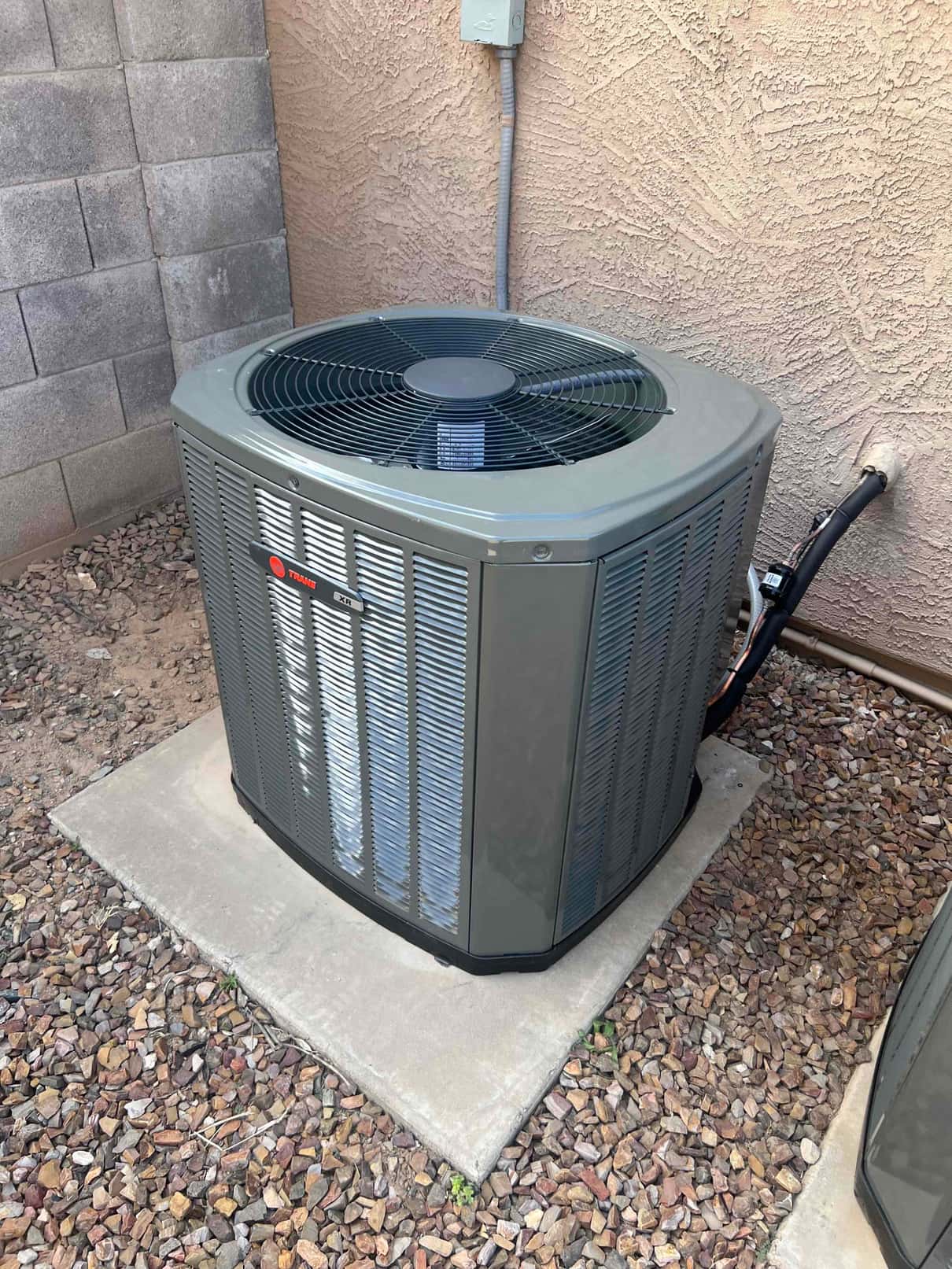 New outdoor condenser set on a level pad with insulated refrigerant lines and weatherproof electrical whip to the disconnect.