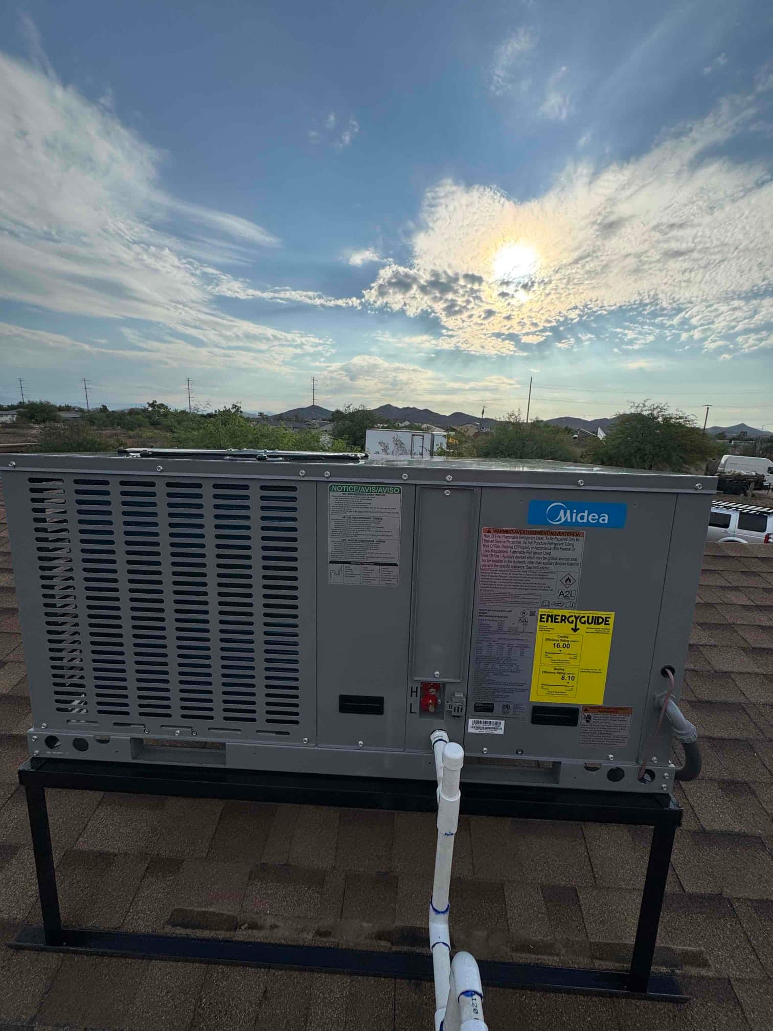 New rooftop package HVAC unit set on a metal stand with connected condensate drain piping and electrical whip.