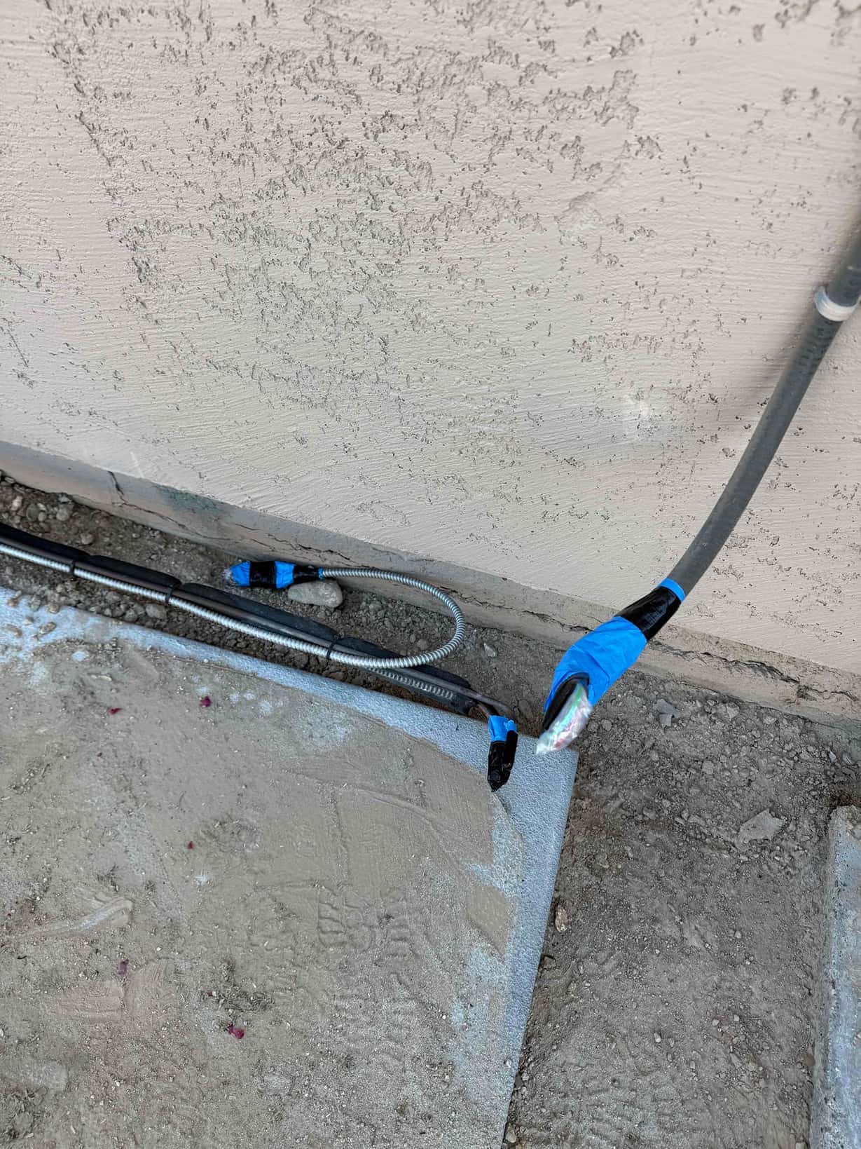 Outdoor condenser pad with routed refrigerant lines, control cable, and armored electrical whip protected with tape before equipment set.
