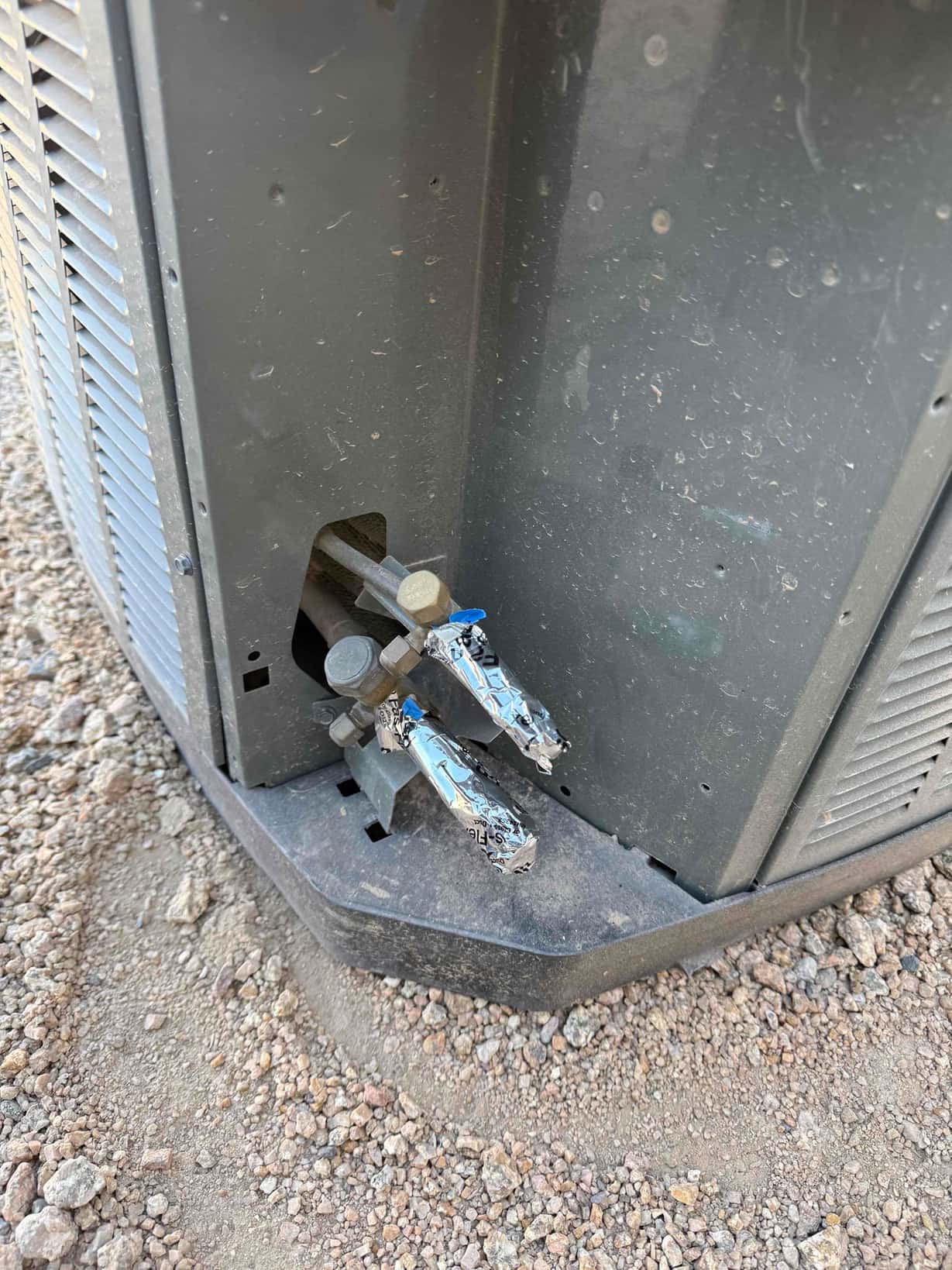 Outdoor condenser service valves and capped refrigerant line connections at the base of the unit during installation.