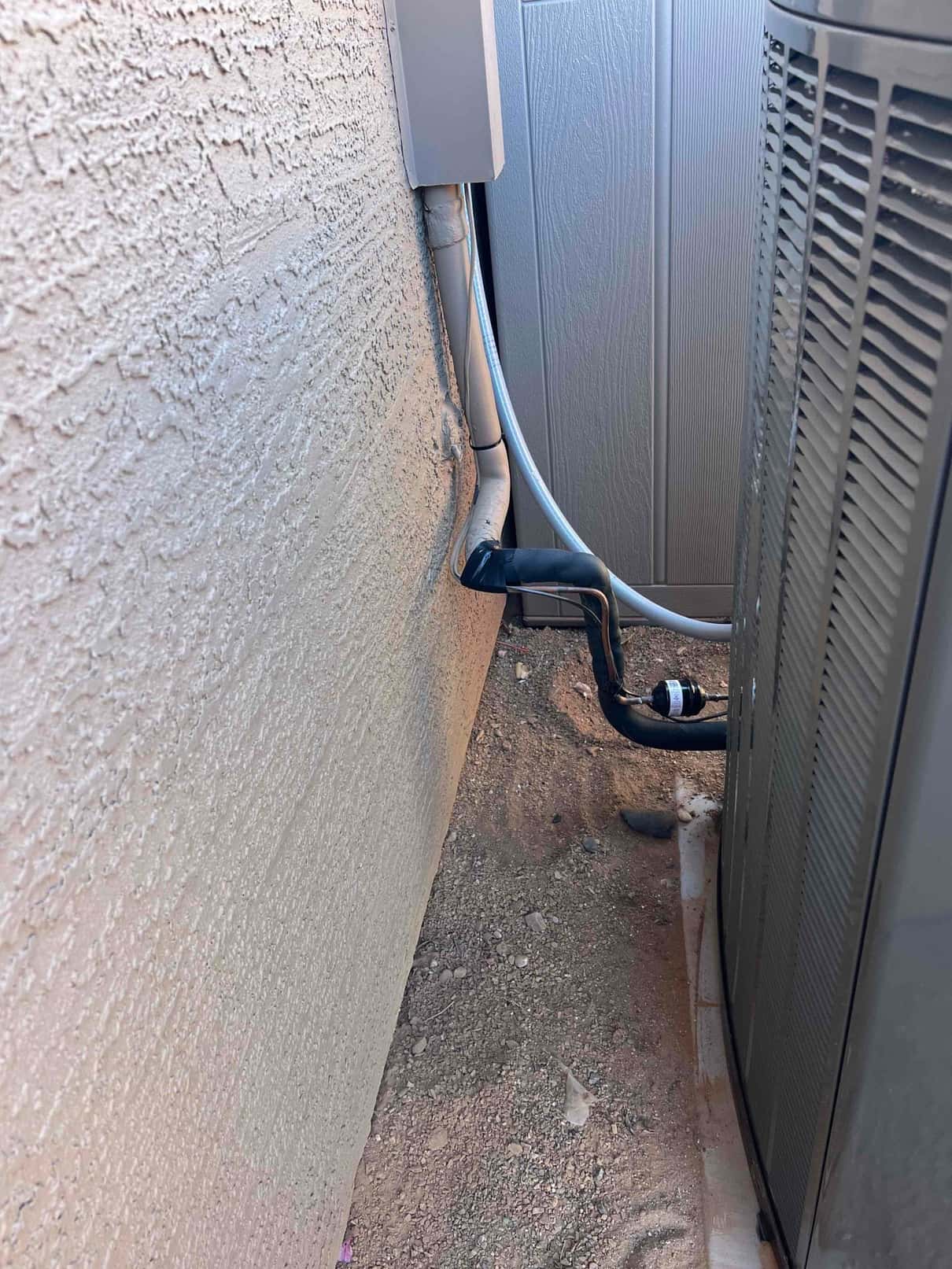Outdoor condenser set beside the wall with insulated refrigerant lines, suction line filter-drier, and electrical whip to the disconnect.