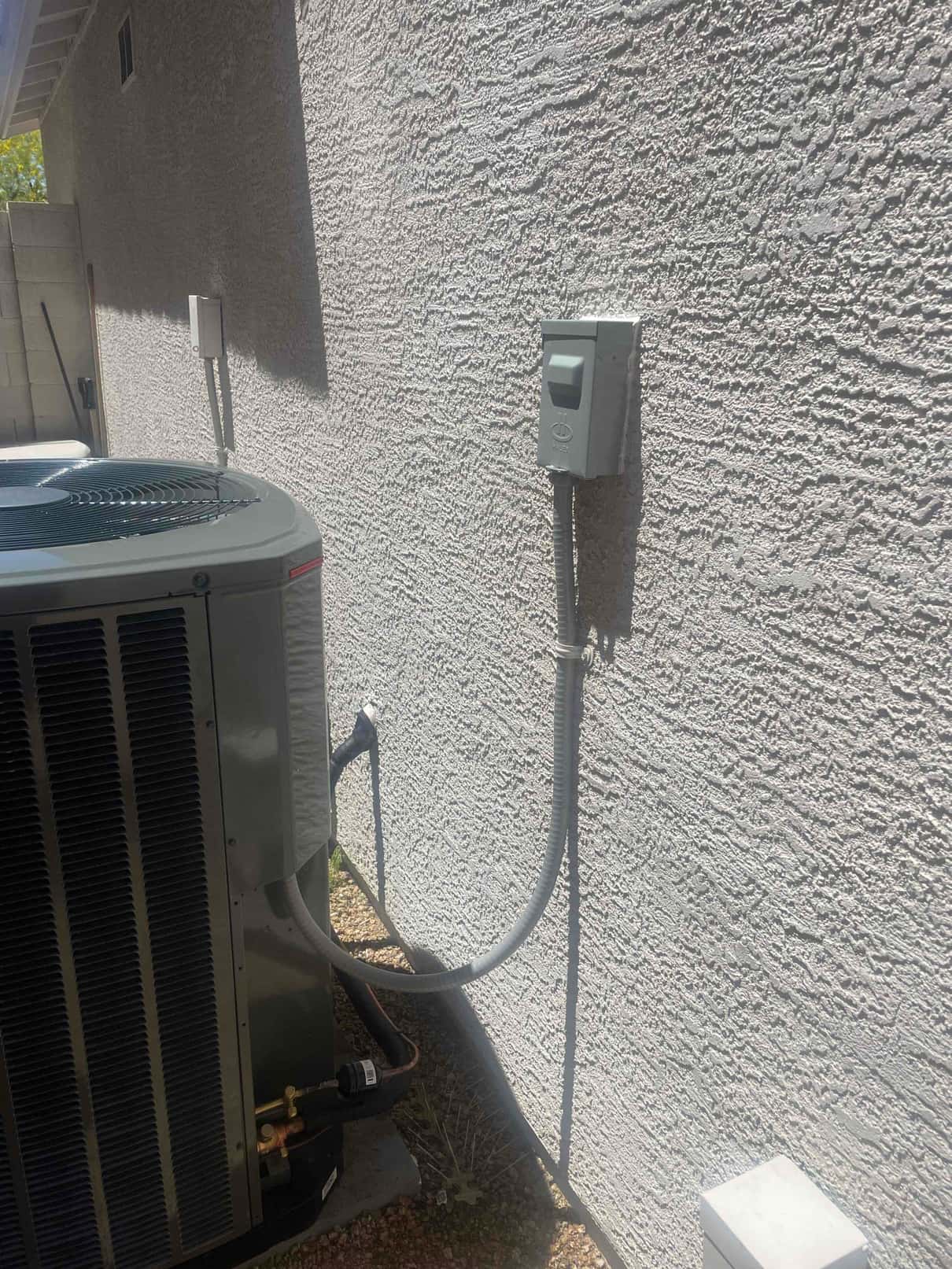 Outdoor condenser set on a level pad with new electrical disconnect and flexible conduit securely mounted to the wall.