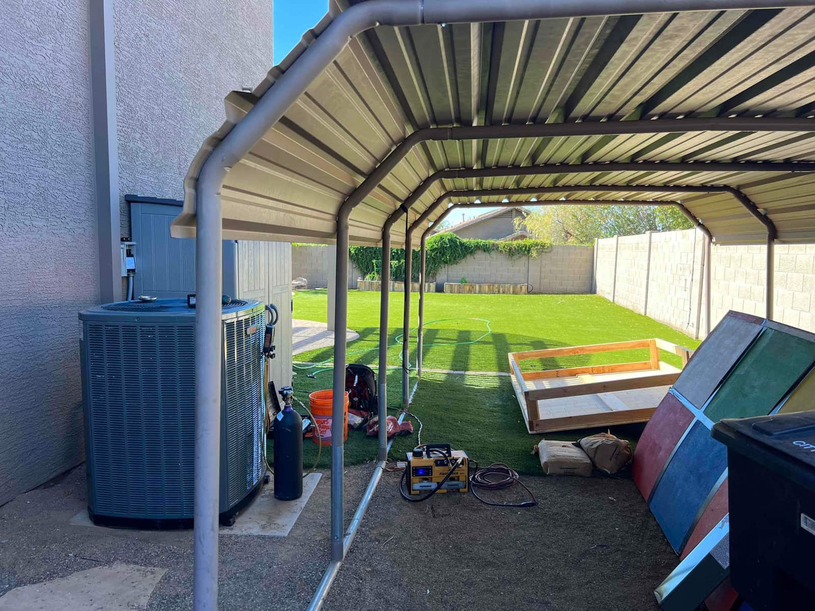 Outdoor condenser set on a pad beside the house with nearby service disconnect and tools staged under a shade structure.