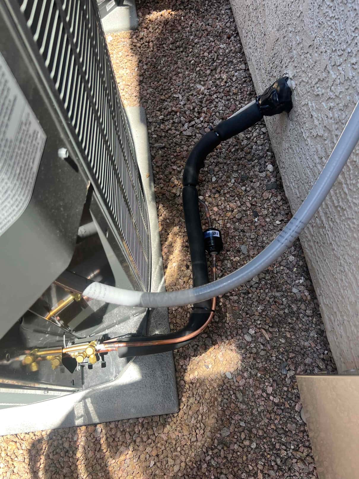 Outdoor condenser set on a pad with insulated suction line, copper line set connections, and sealed wall penetration at the entry.