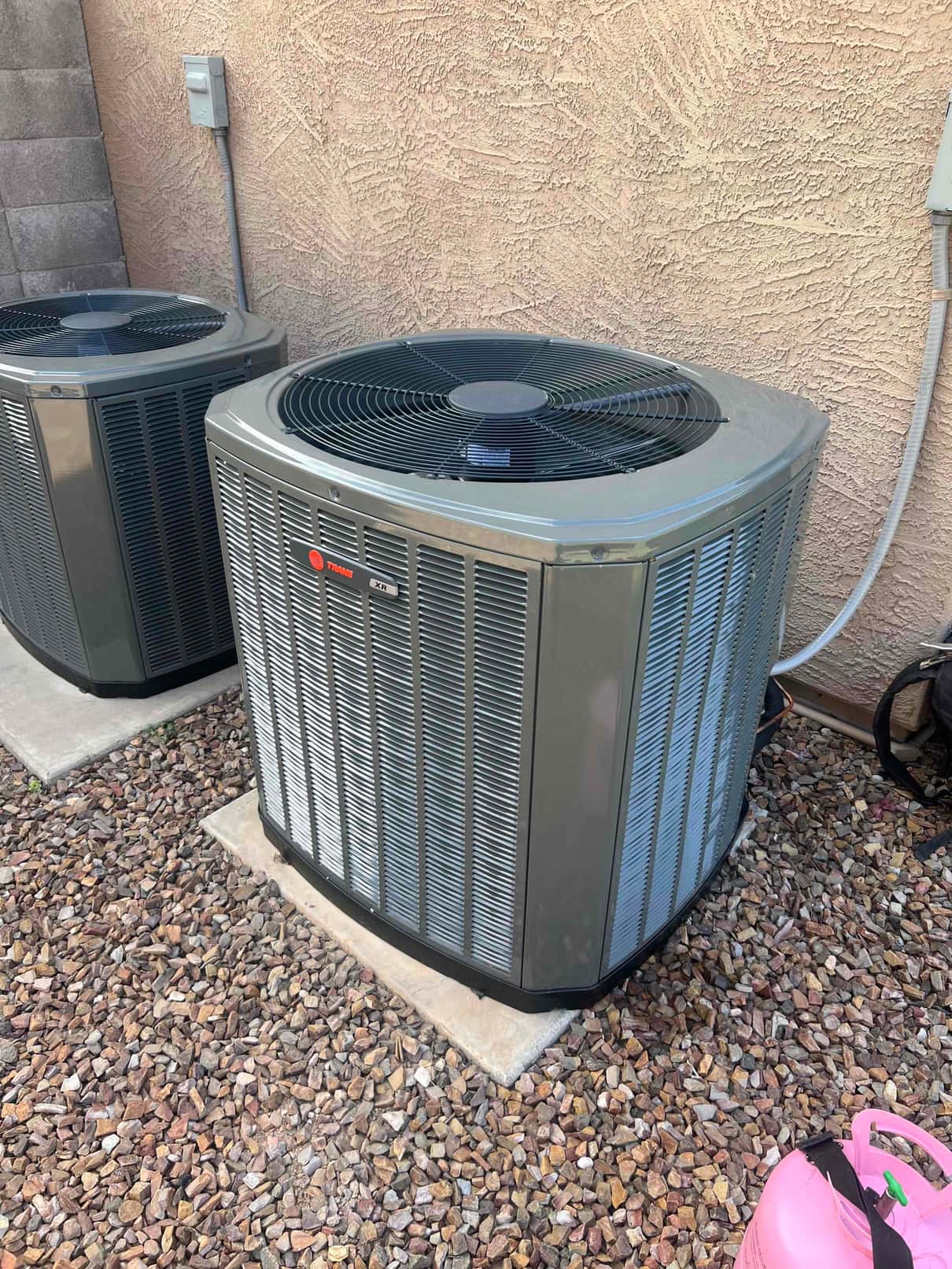 Two outdoor condensers set on level pads with electrical disconnects mounted on the wall and refrigerant lines routed.