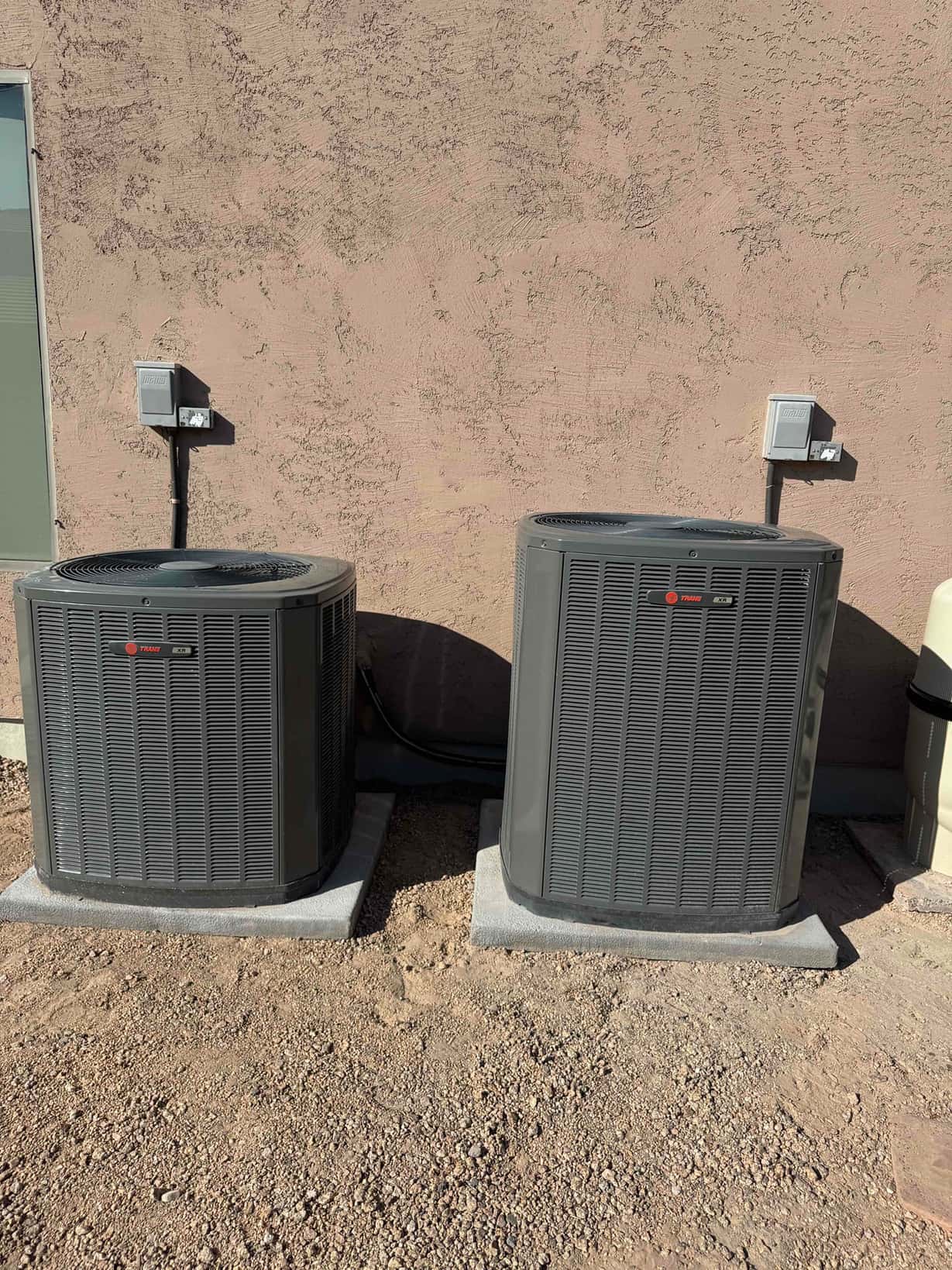 Two outdoor condensers set on level pads with insulated line sets and dedicated disconnect boxes mounted on the wall.