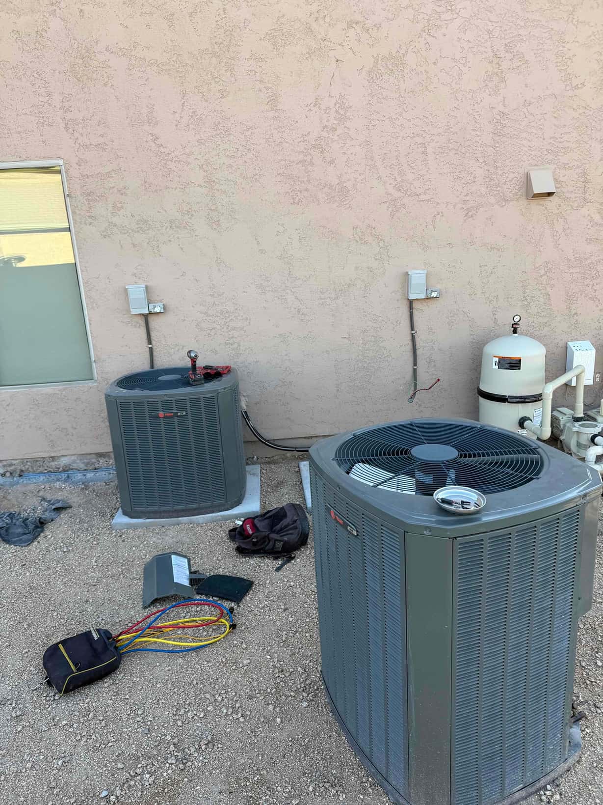 Two outdoor condensers set on pads with disconnect boxes mounted on the wall and tools staged for installation work.