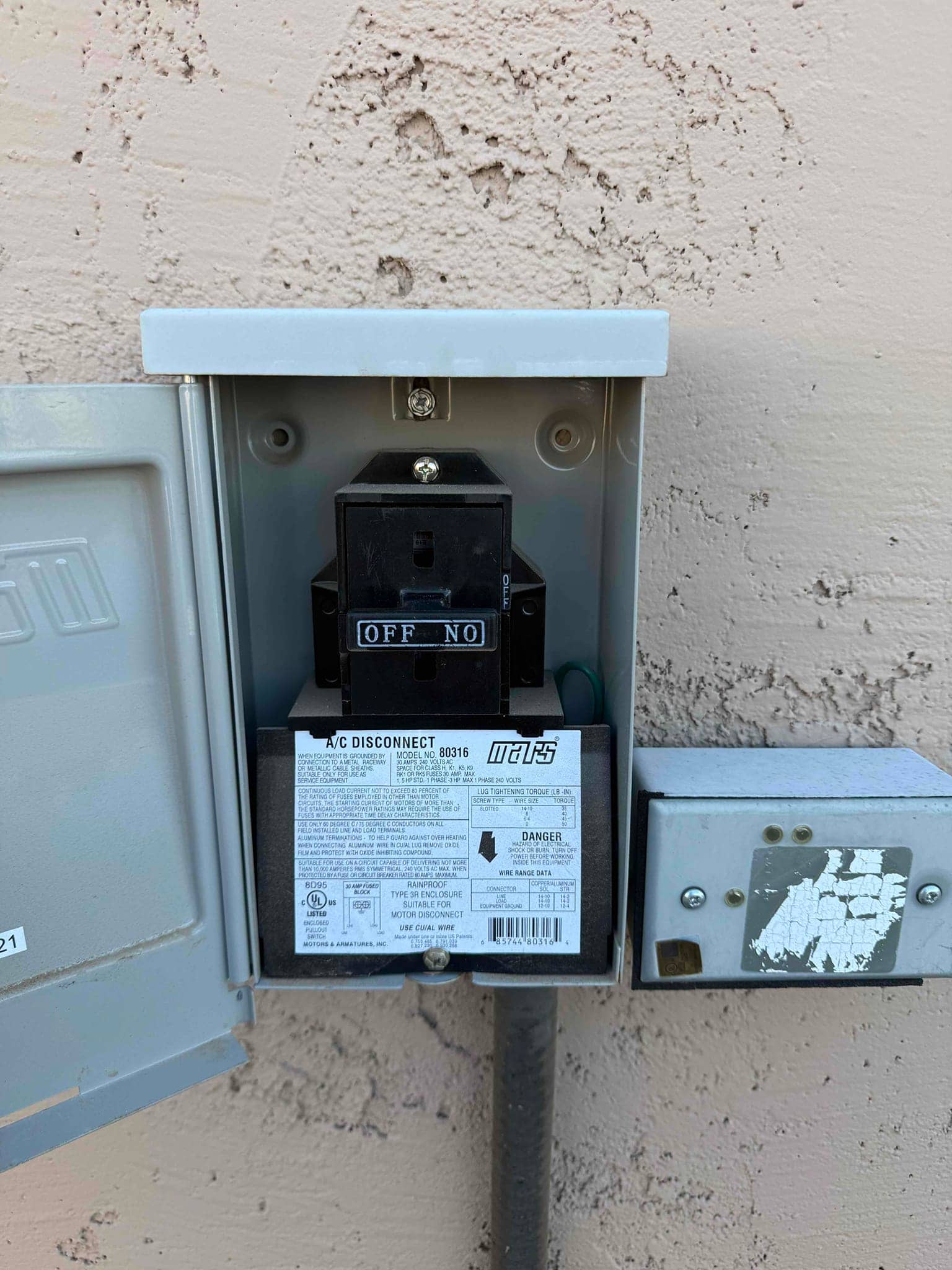 Outdoor A/C disconnect with pull-out switch in the OFF position, cover open to show enclosure and conduit connection.