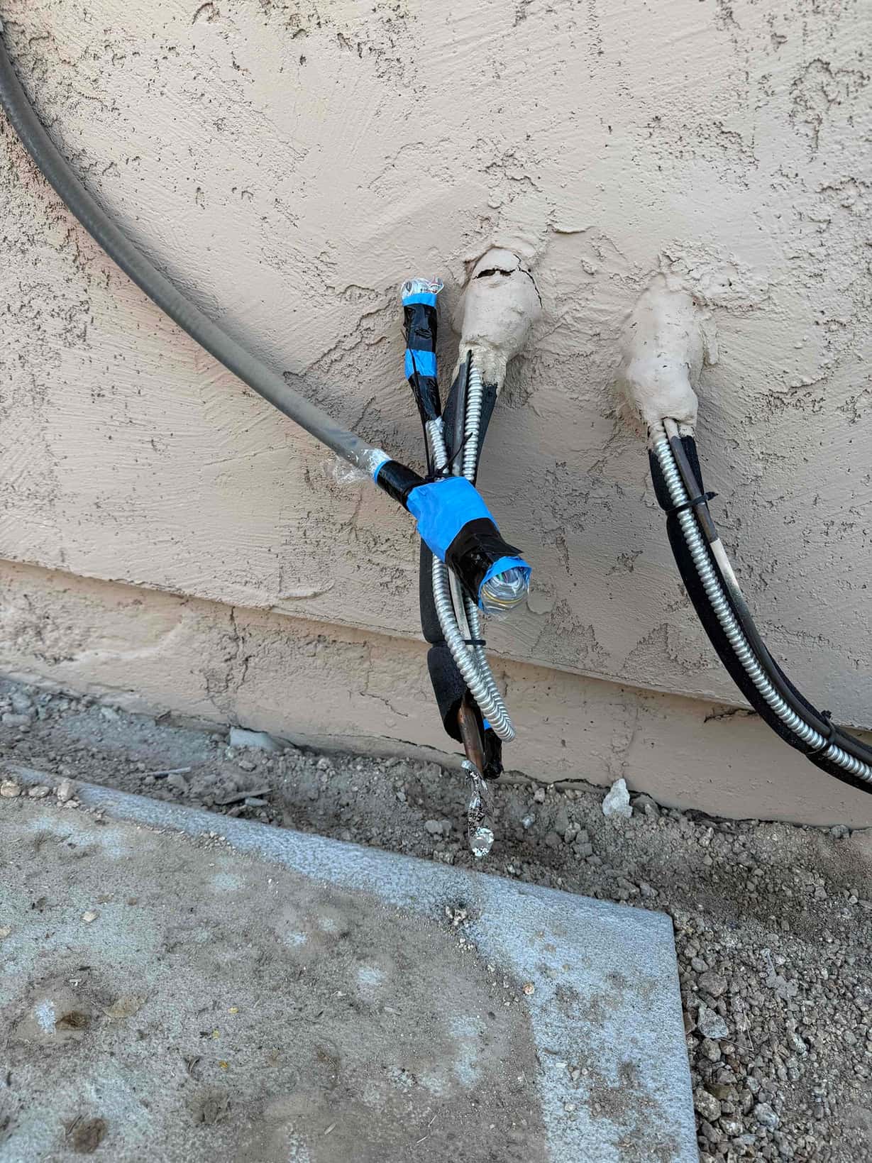 Refrigerant lines, control wiring, and electrical whip routed through sealed wall penetrations, prepped with tape and insulation at the condenser location.