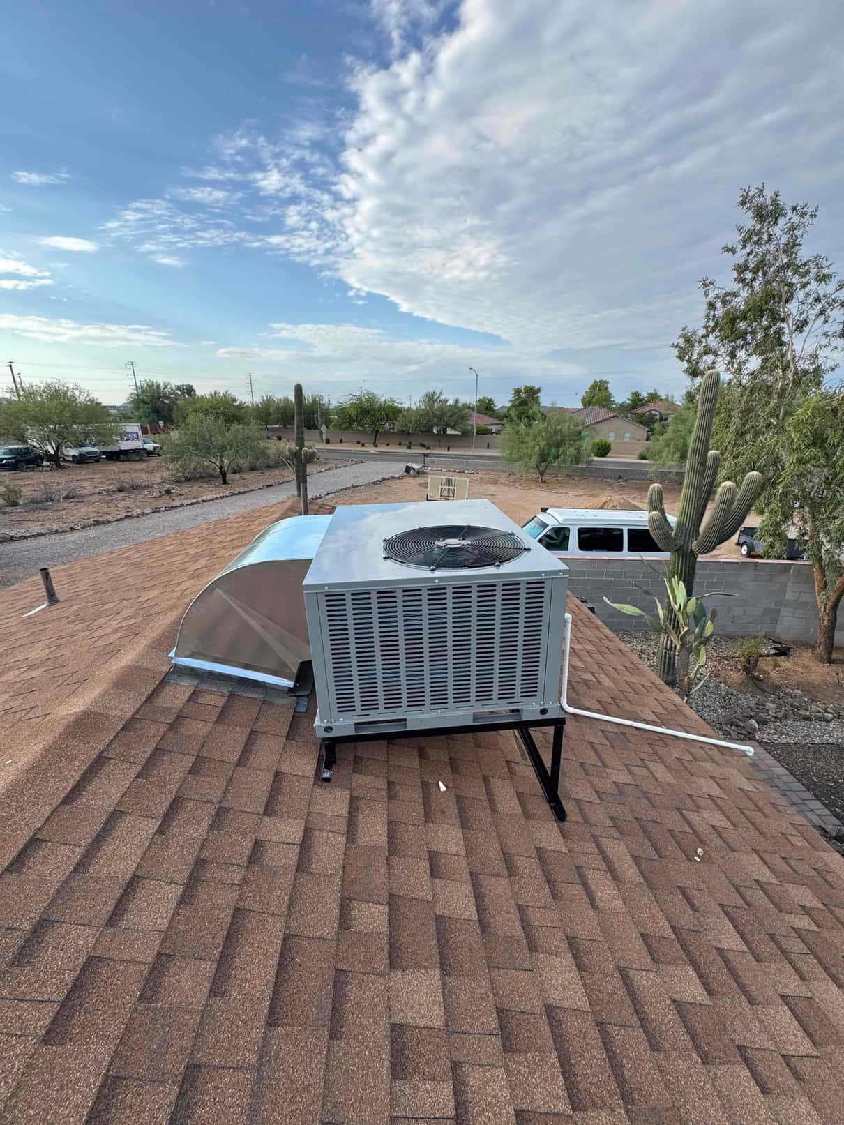 Rooftop package unit newly installed on a stand with connected supply/return duct transition and condensate drain routing across shingles.