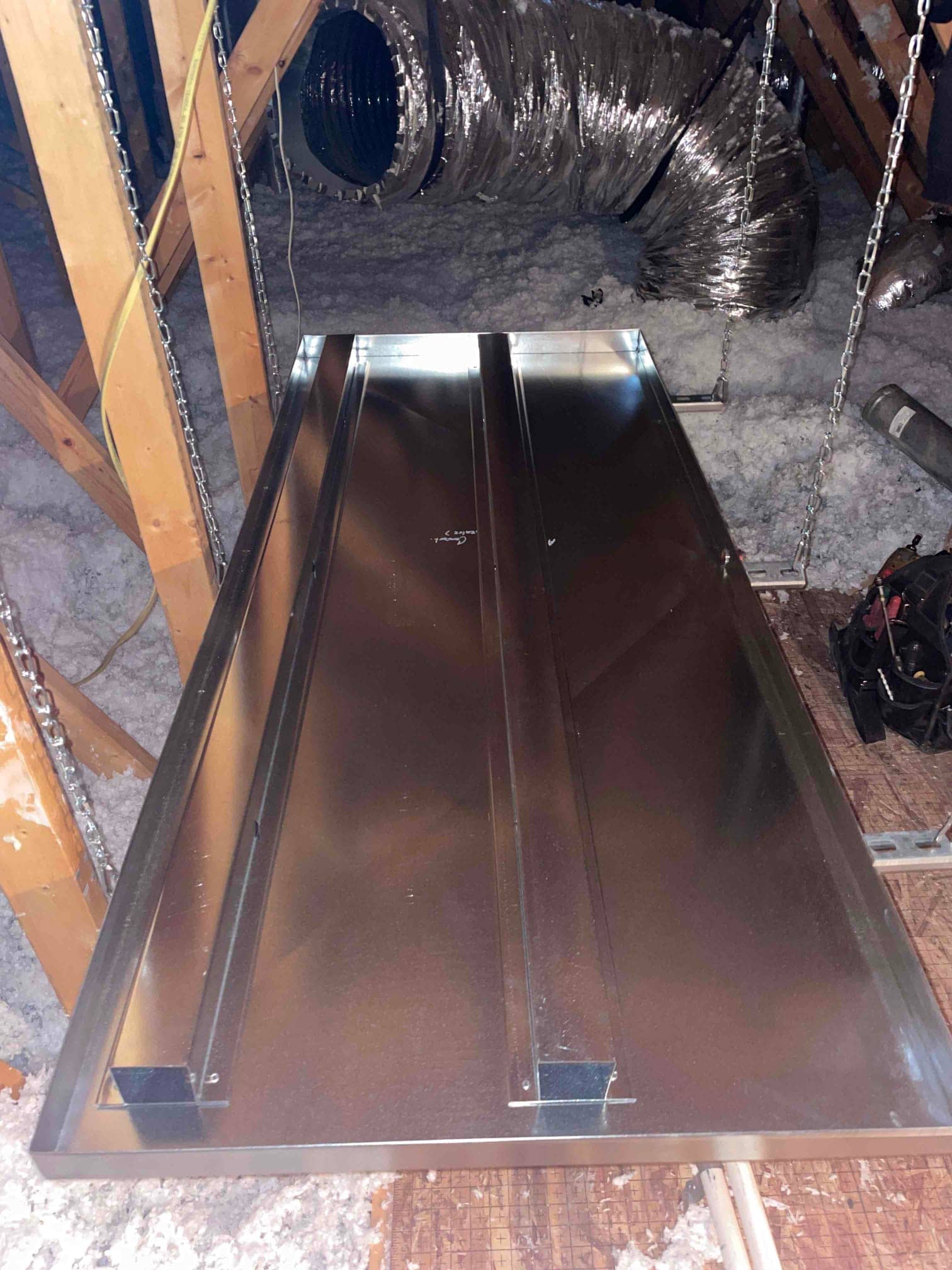Sheet-metal equipment platform suspended with chains in the attic near insulated flexible ductwork and ceiling insulation.