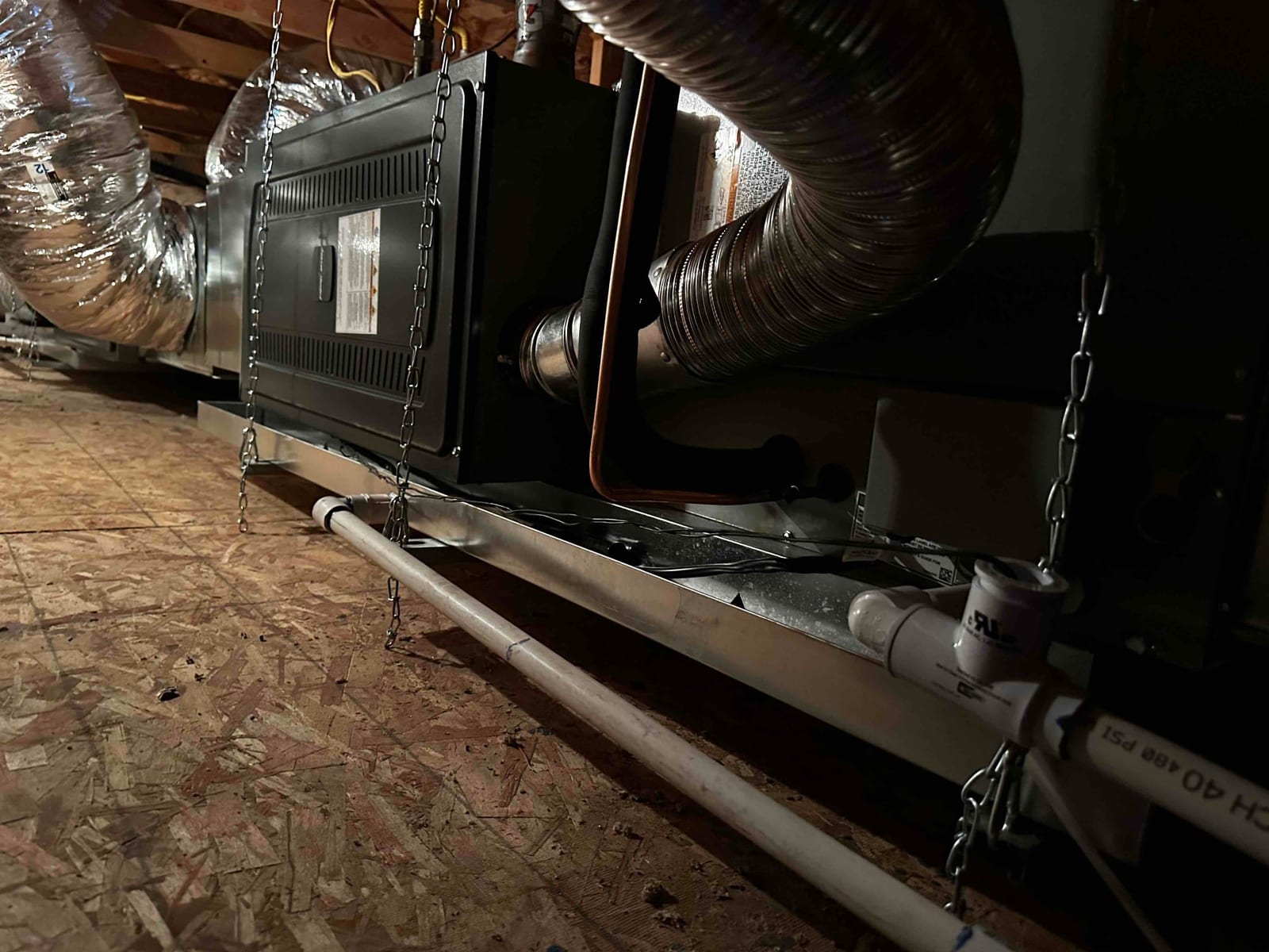 Suspended horizontal air handler with insulated ducts, metal drain pan, and PVC condensate piping installed in an attic space.