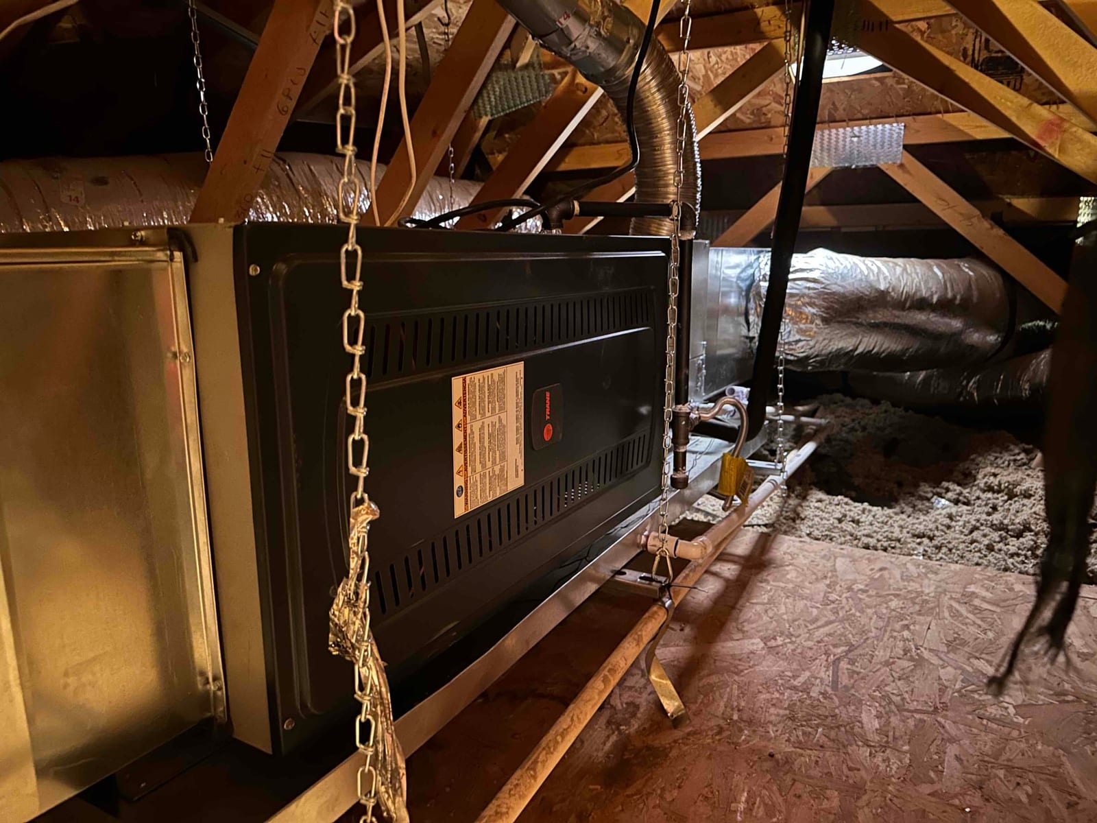 Suspended horizontal furnace and coil installed in attic with insulated ductwork, drain line, hanging chains, and service platform visible.