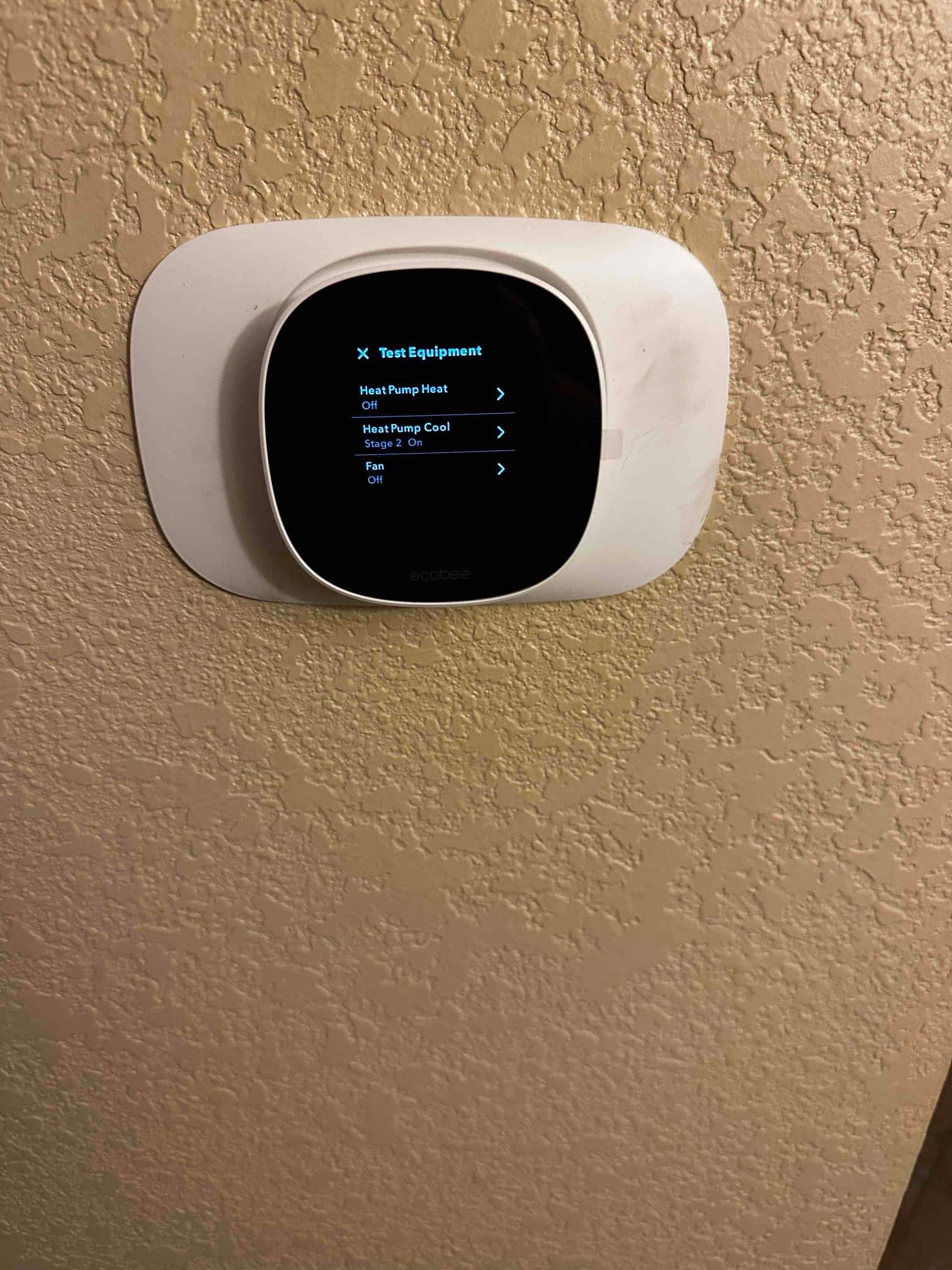 Thermostat on wall showing test equipment menu with heat pump cool stage 2 on and fan off.