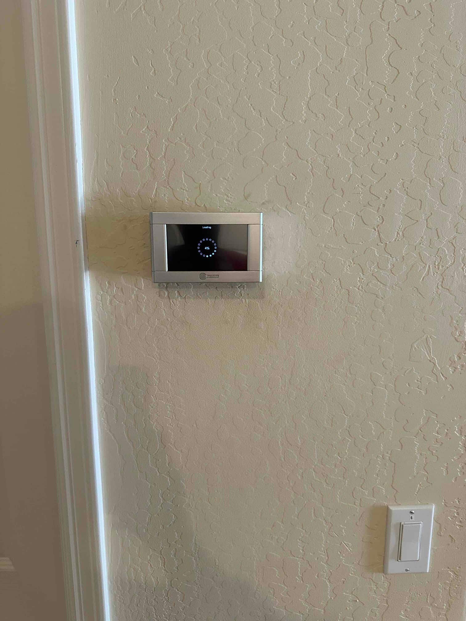 Wall-mounted digital thermostat installed and powered on, adjacent to a light switch on a textured interior wall.