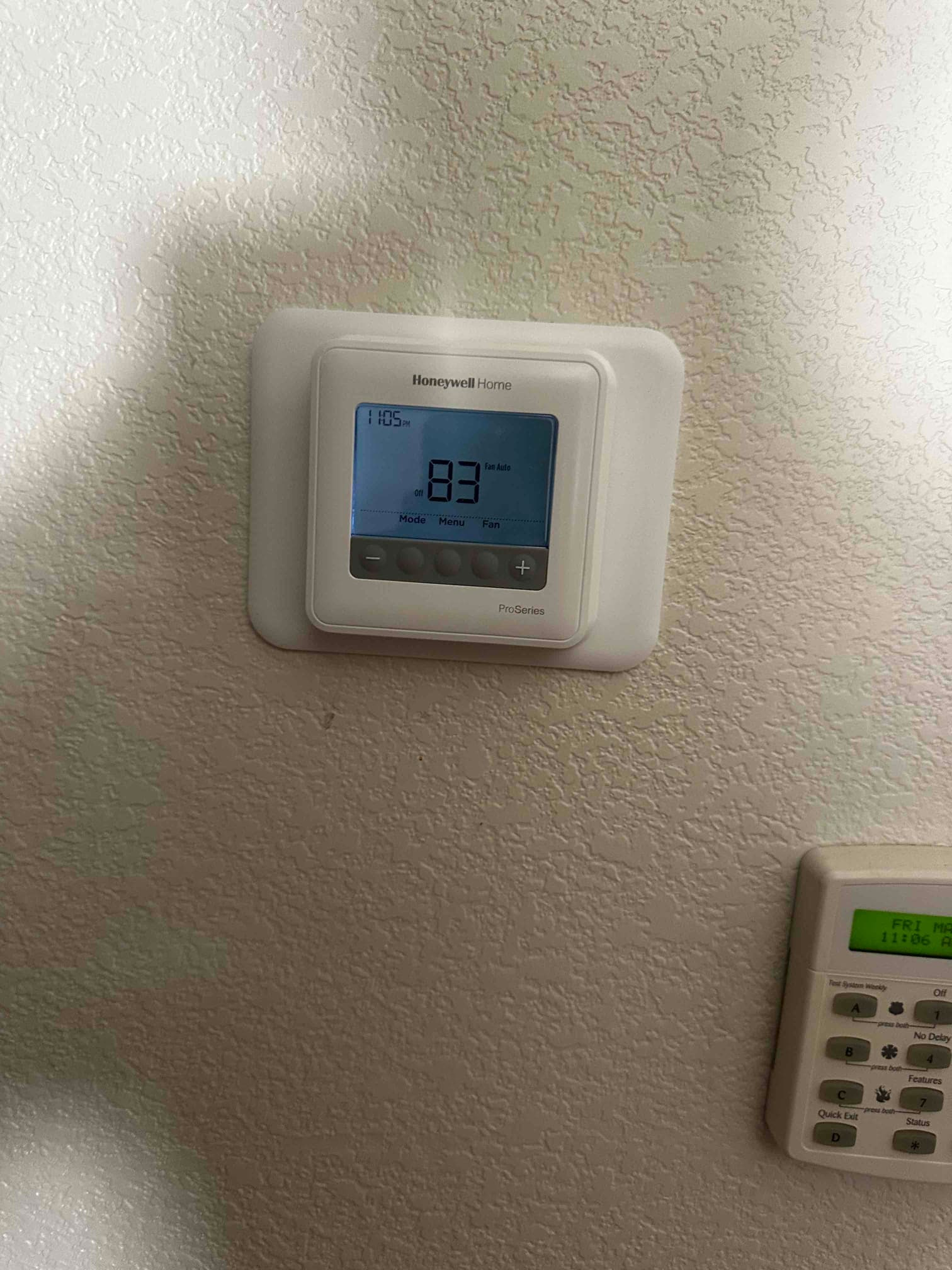 Wall-mounted digital thermostat installed and powered on, displaying room temperature and control options in a residential interior.