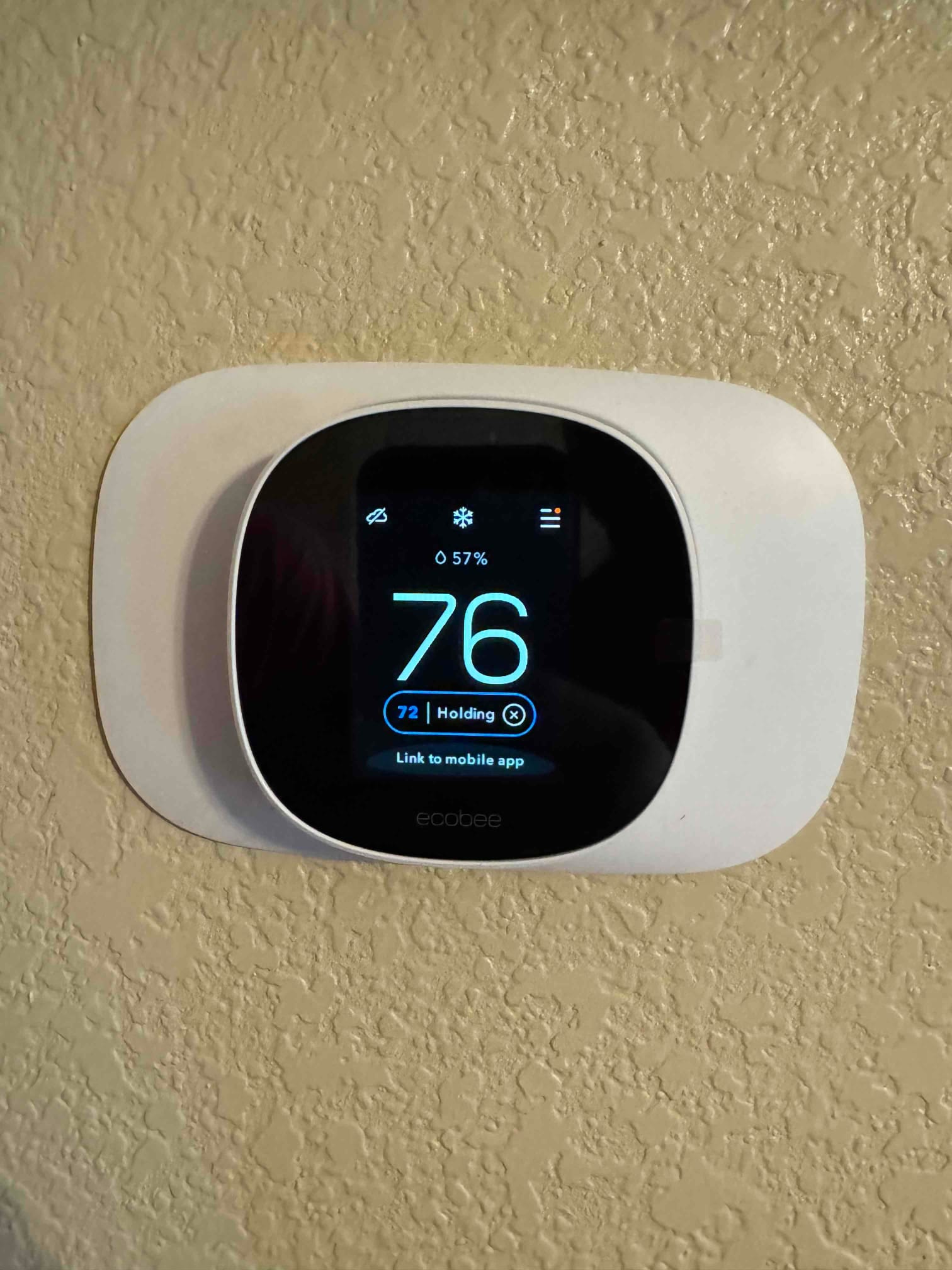 Wall-mounted smart thermostat installed and operating, display showing cooling mode with indoor temperature reading 76 degrees.