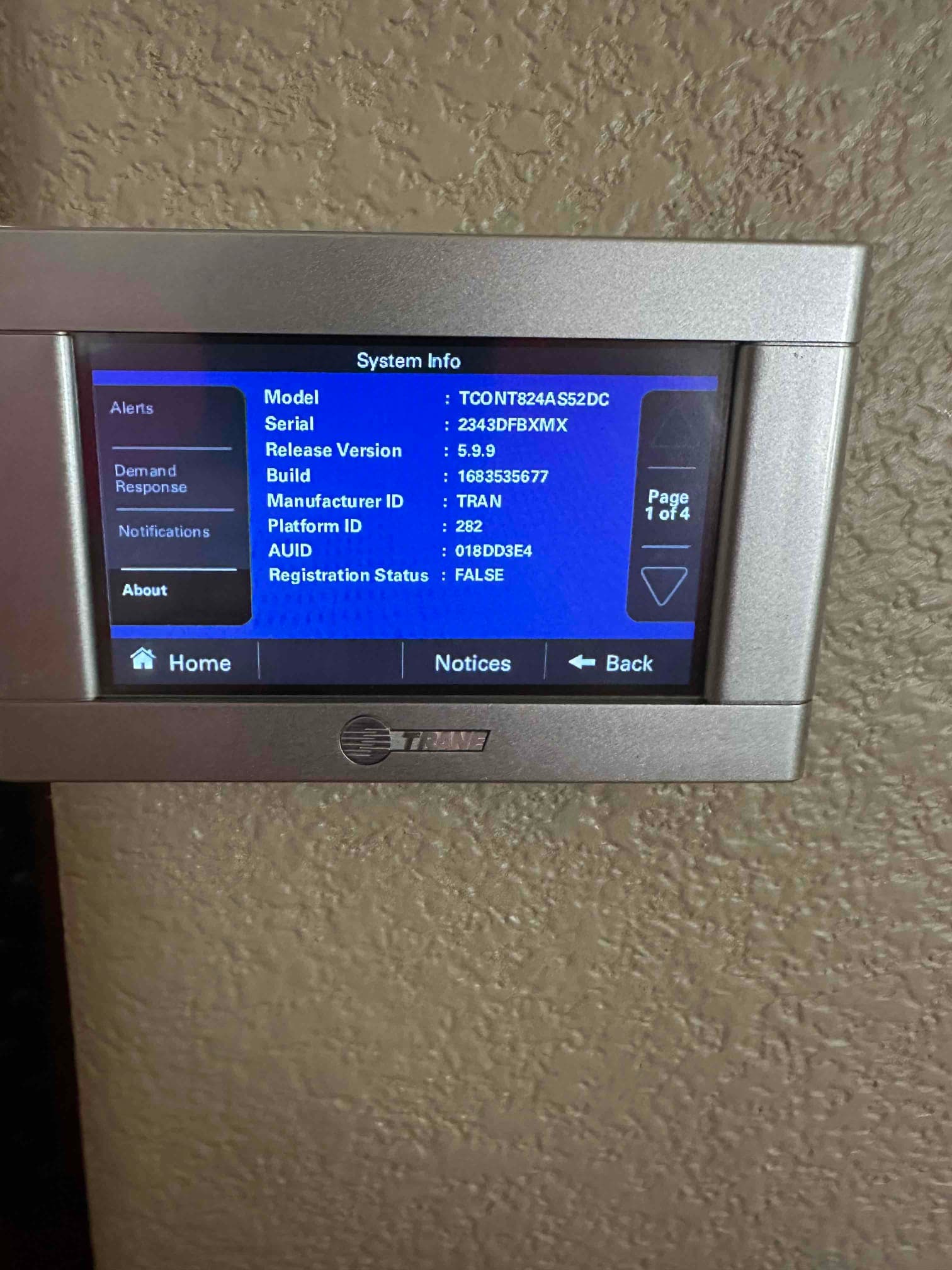 Wall-mounted thermostat displays system information screen during setup, showing model, serial, and software details for the newly installed controls.