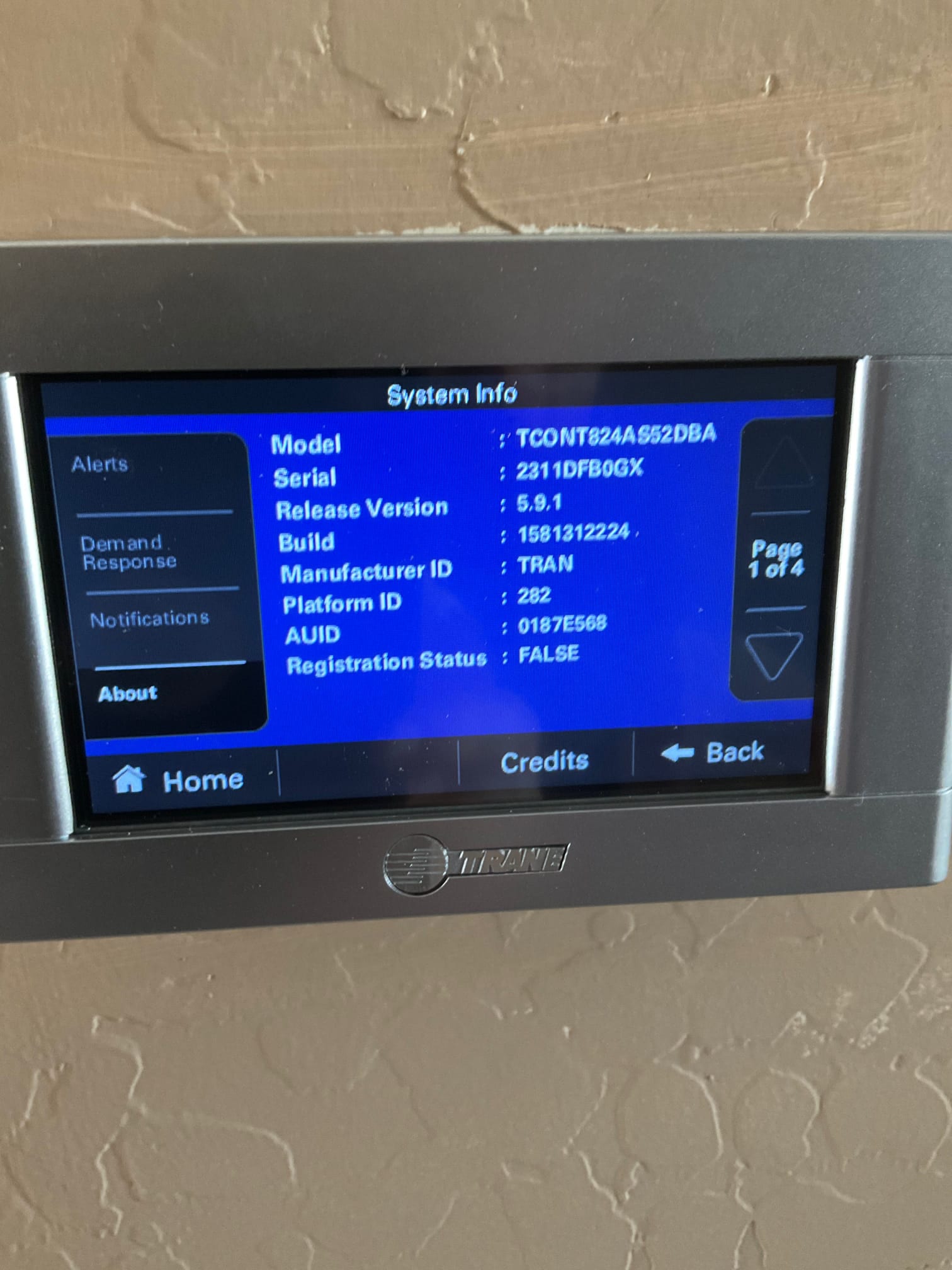 Wall-mounted touchscreen thermostat displays system information menu after installation, showing model, serial, software version, and registration status.