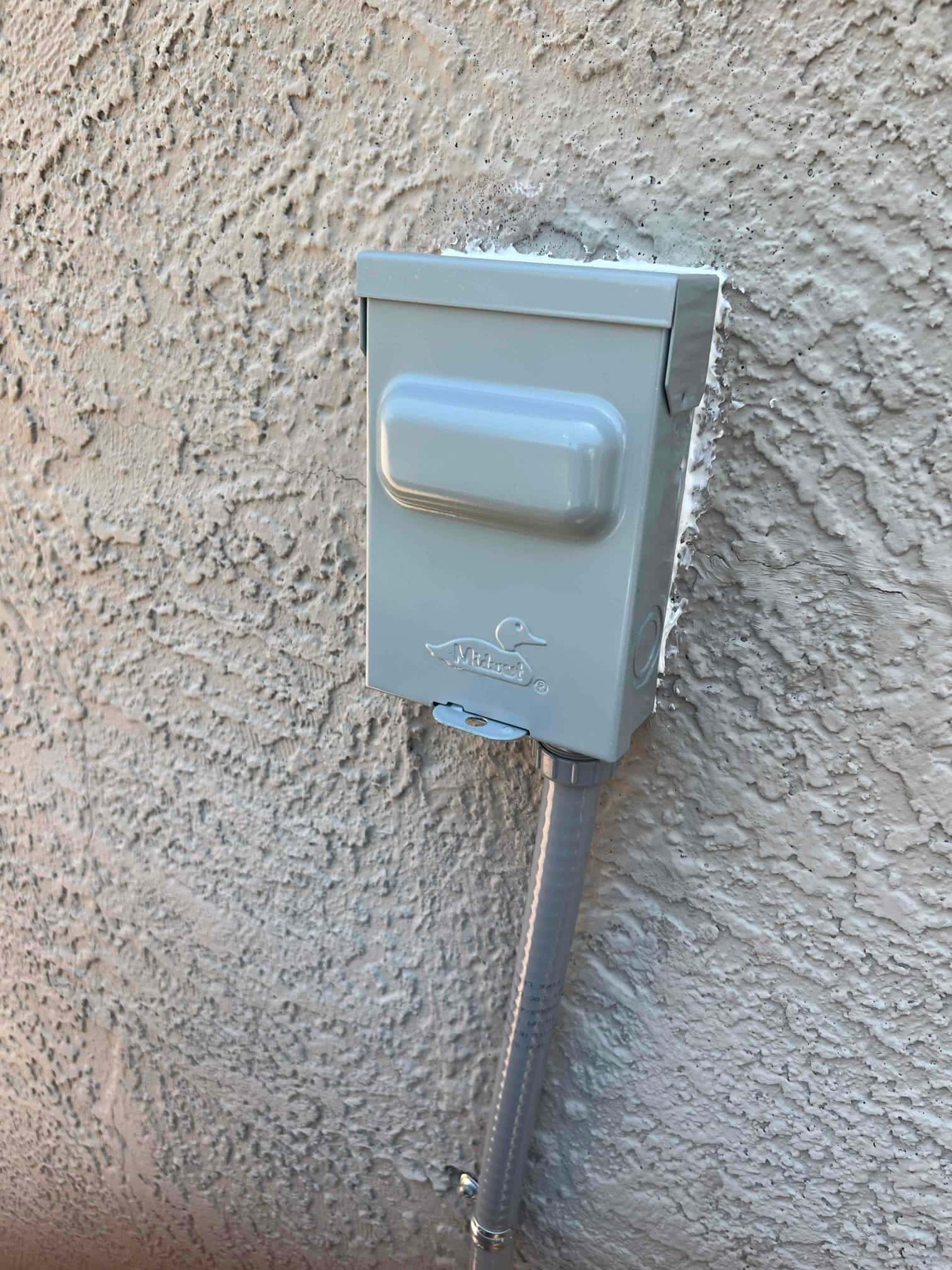 Weatherproof HVAC service disconnect mounted on exterior wall with sealed penetration and flexible conduit routed downward.