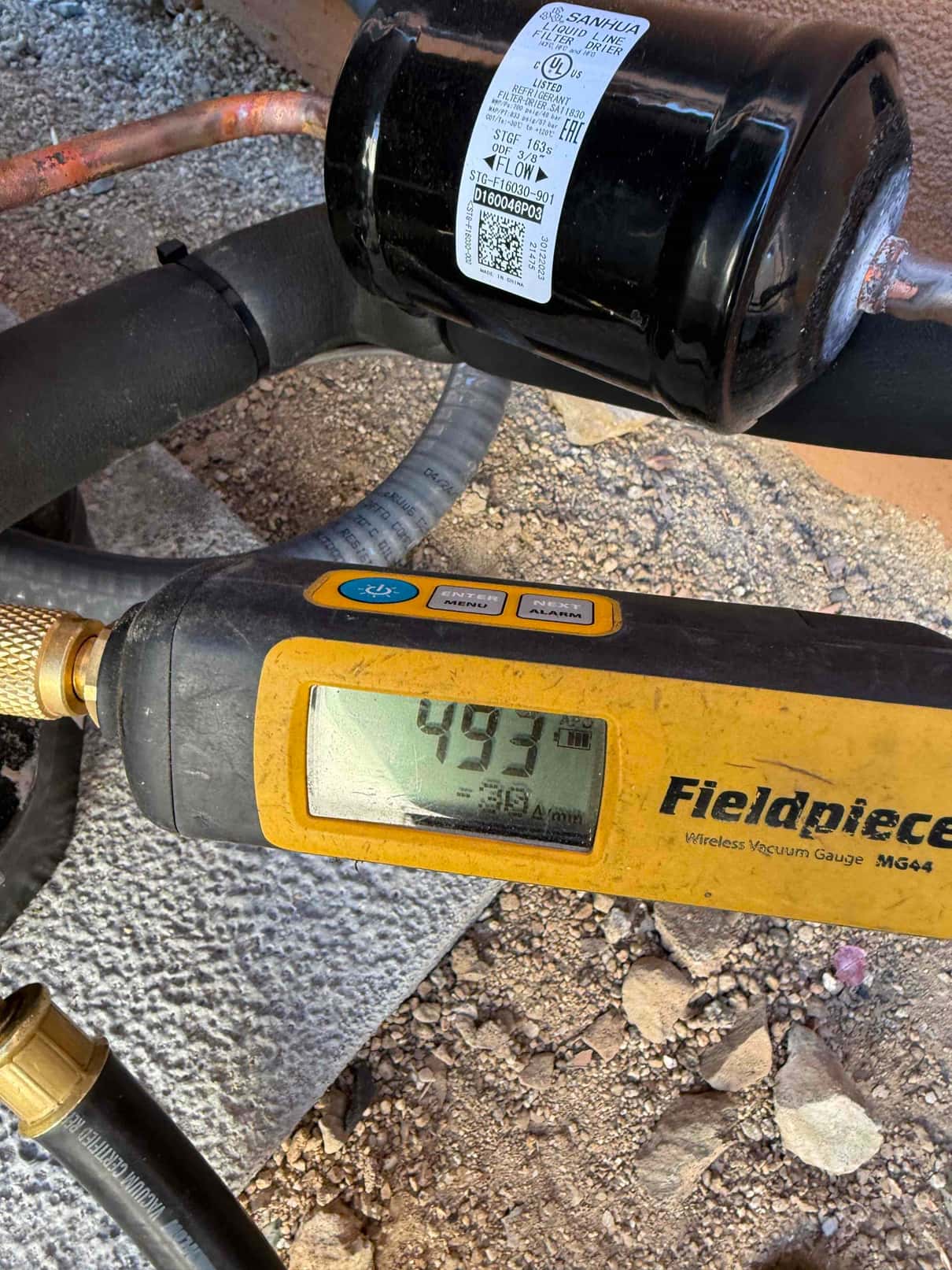 Wireless micron gauge shows 493 microns during system evacuation beside a newly installed liquid-line filter drier.