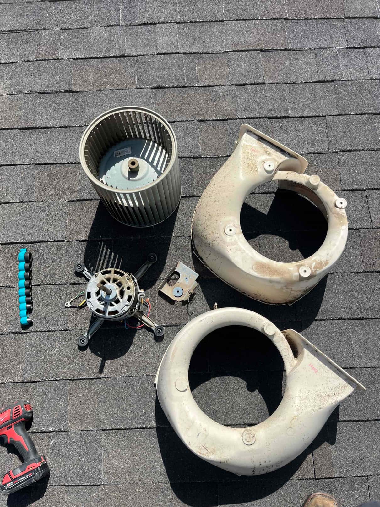 Blower wheel, motor assembly, and plastic housings removed for service, laid out on a roof with tools nearby.