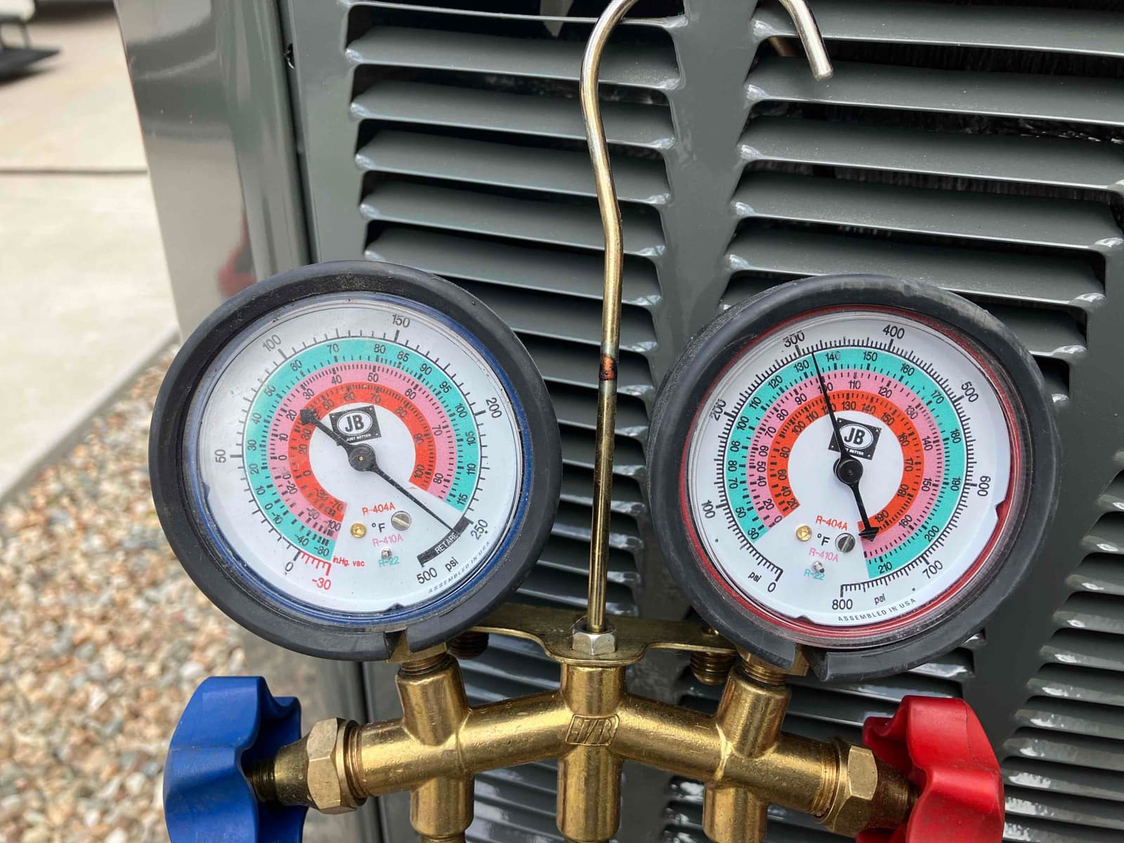 Analog manifold gauges show equal high pressure on both sides during a nitrogen pressure test at the outdoor condenser.