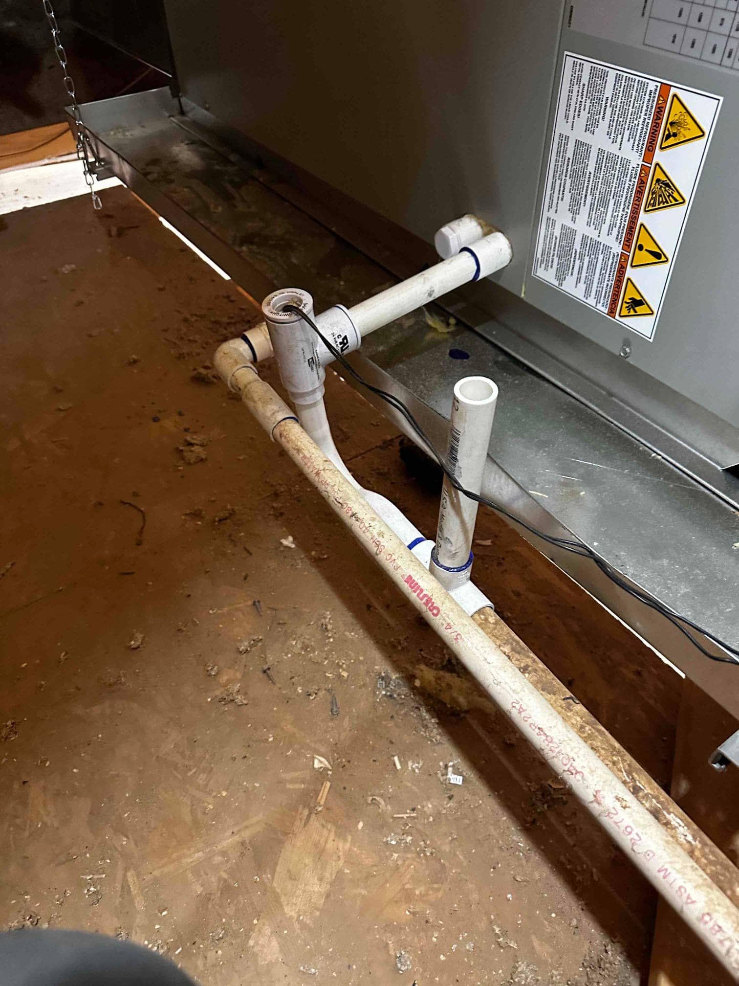 Condensate drain assembly with cleanout and trap connected to the air handler, with wiring routed along the drain pan edge.