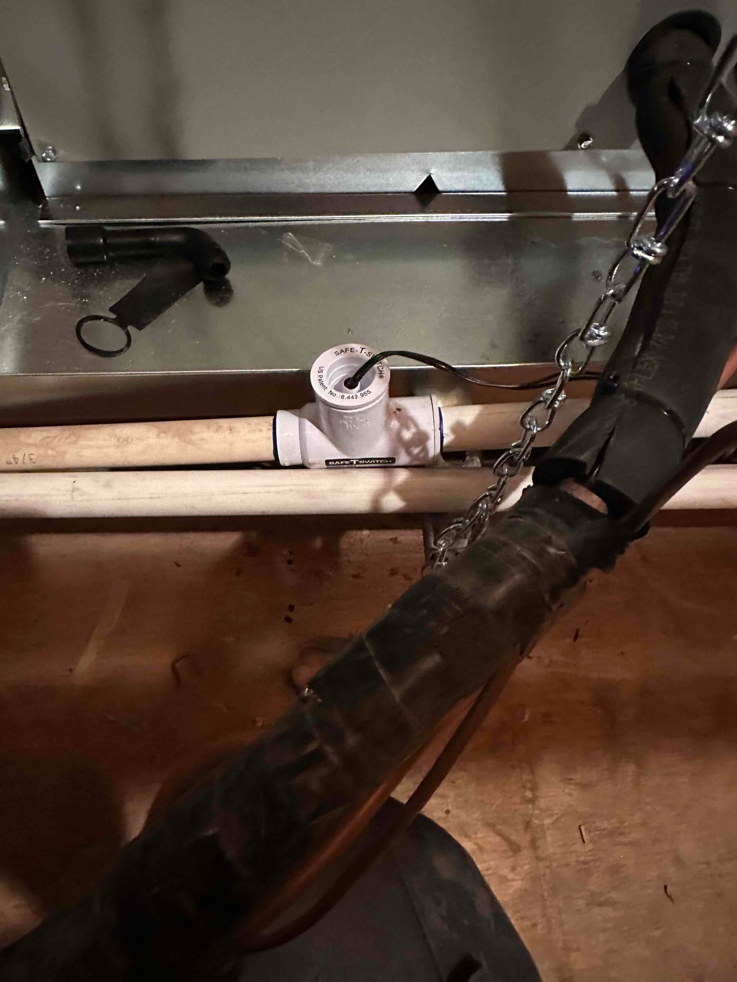 Condensate drain line with float switch installed beneath an air handler, showing proper piping and access panel above.